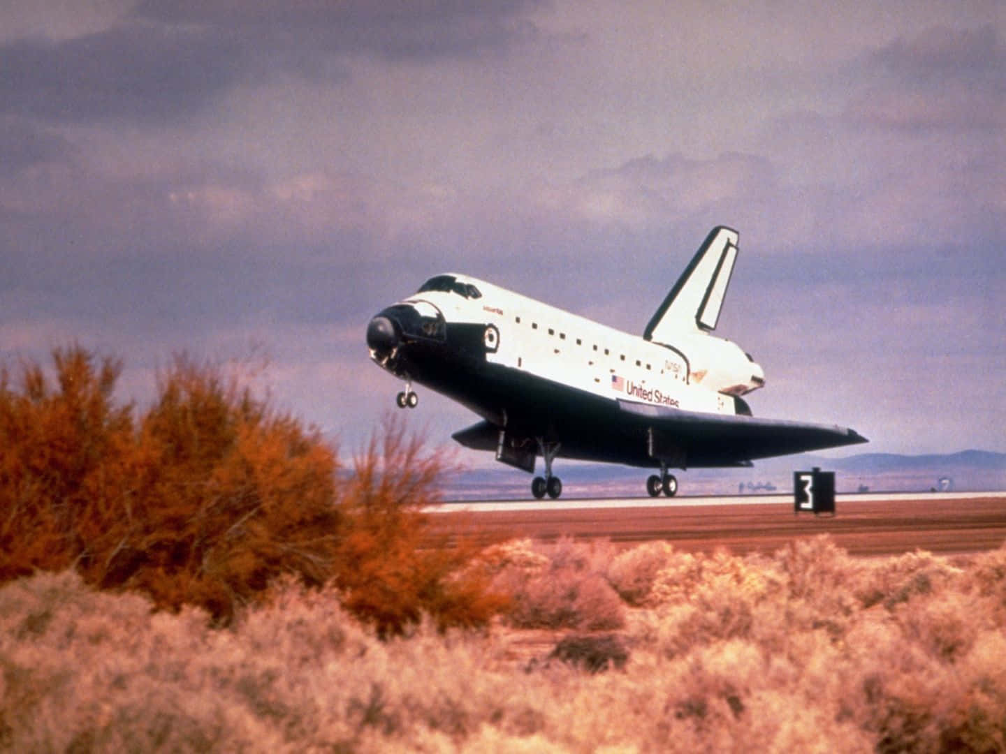 NASA 太空穿梭機降落在沙漠跑道，周圍有灌木和陰天。