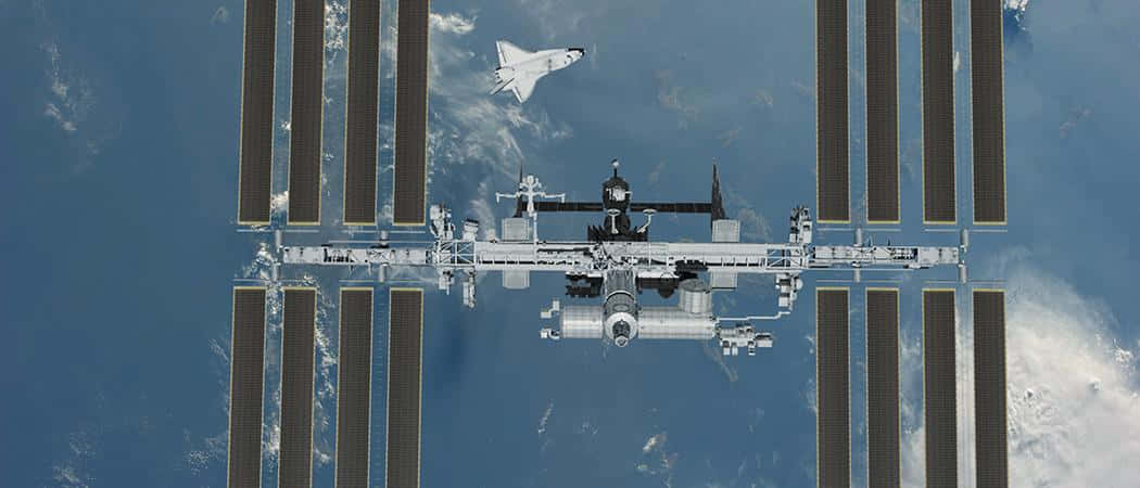 International Space Station 桌布 壁紙 — 一架太空穿梭機正在地球的藍色海洋和白色雲層上方接近國際太空站。