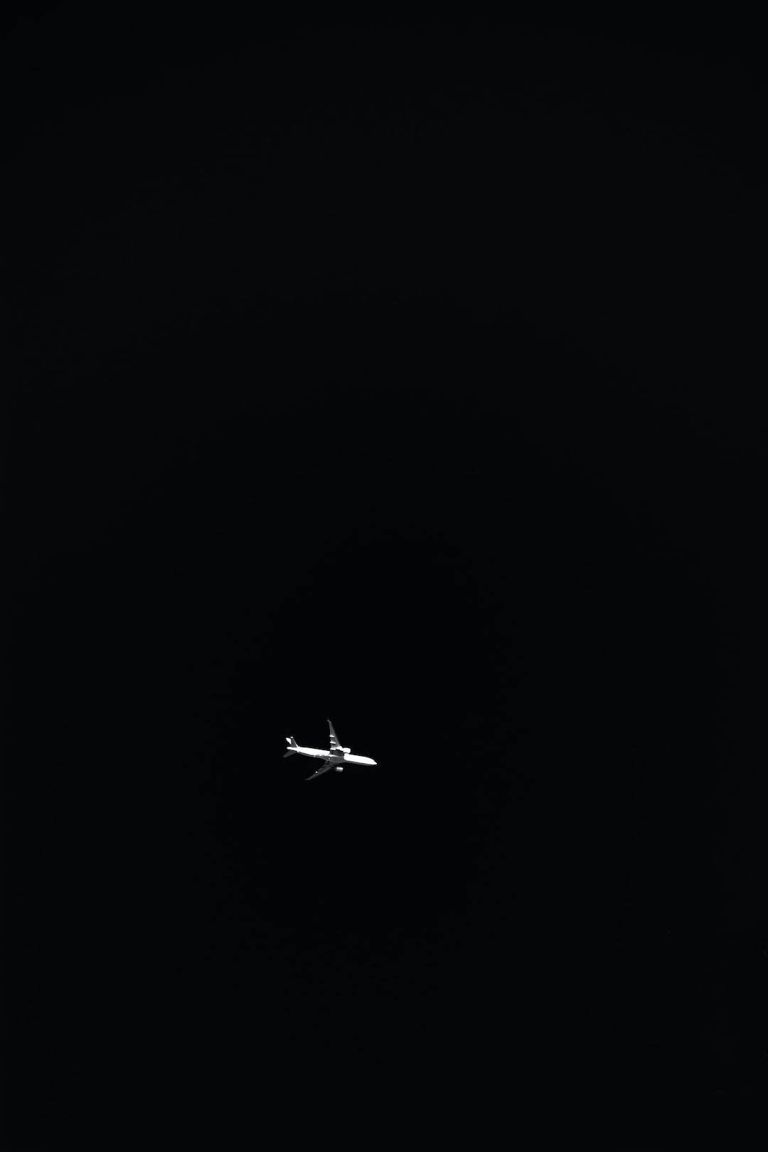 黑白 桌布 壁紙 — 一架孤獨的白色飛機在漆黑的夜空中滑翔，是廣闊黑暗中的一個孤獨小點。