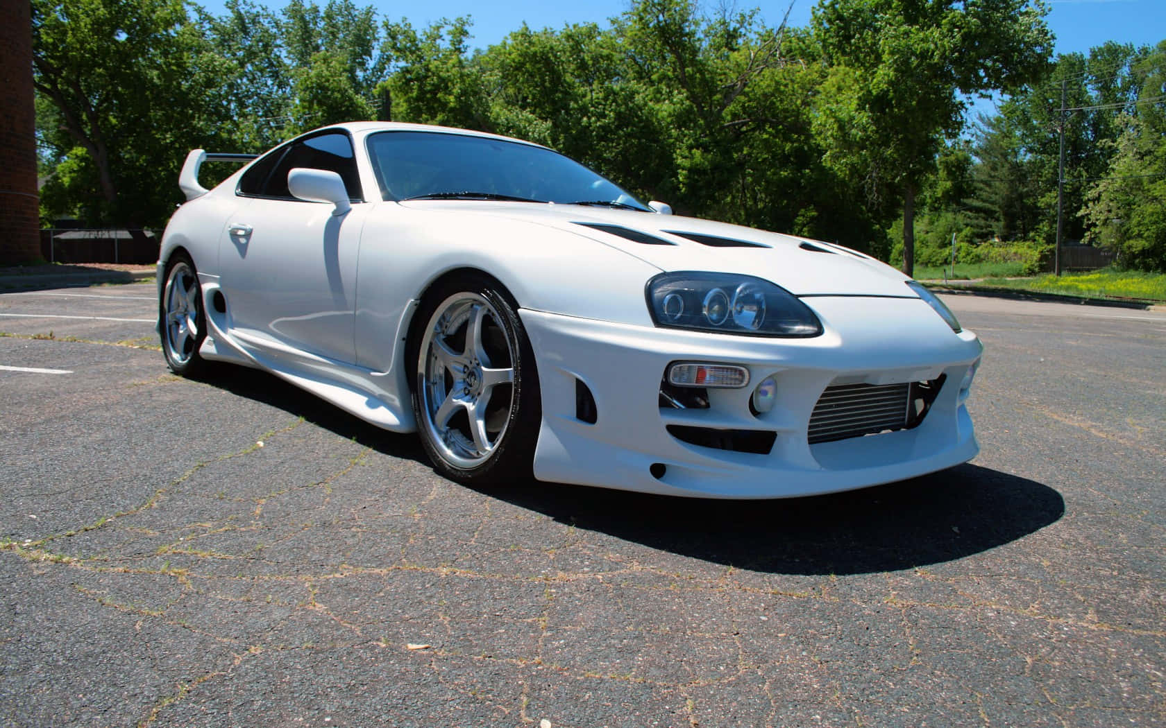 Supra 桌布 壁紙 — 一架完美無瑕的白色豐田Supra跑車停泊在陽光普照的瀝青停車場，背景是茂密的綠樹。