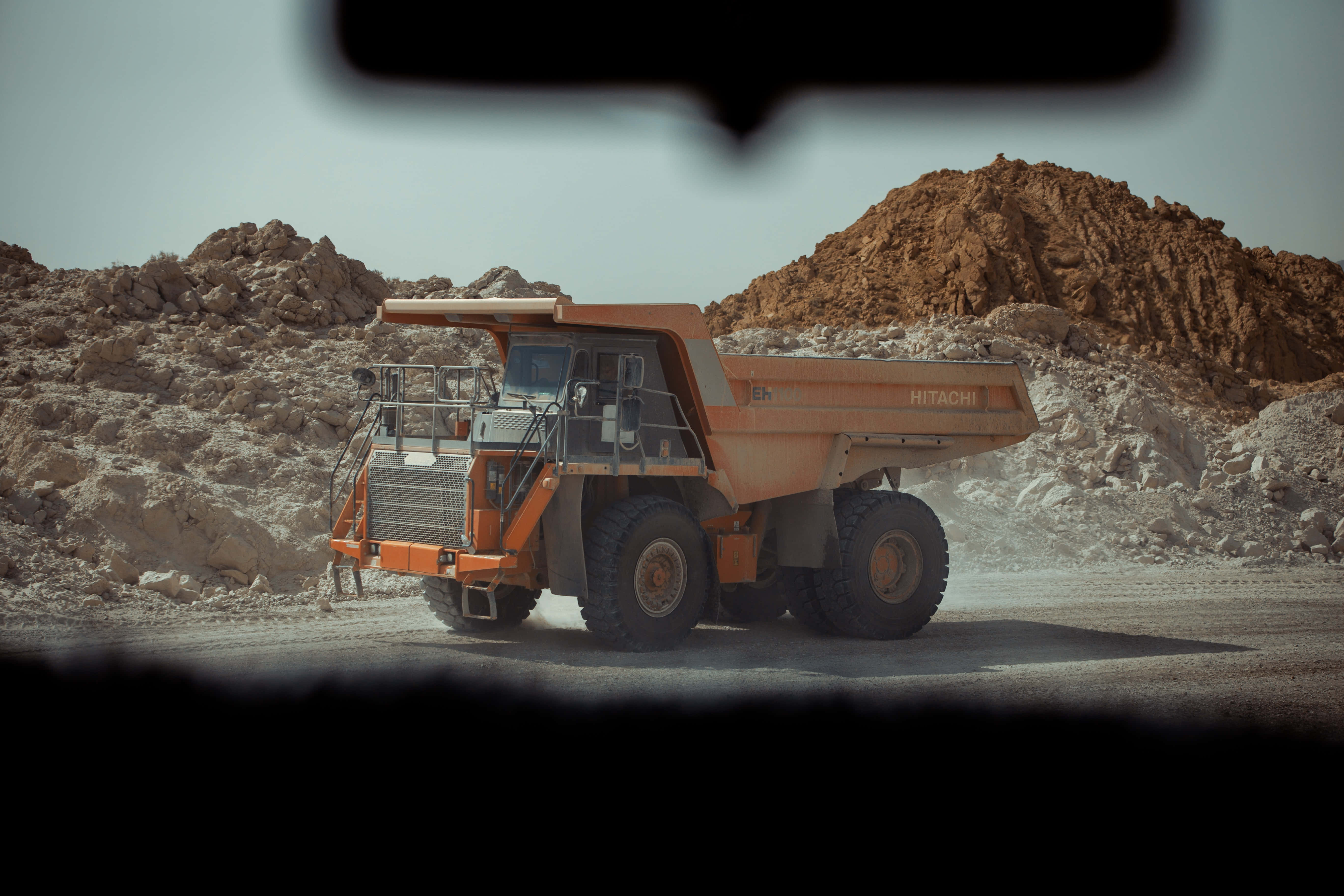 Mining 桌布 壁紙 — 一架巨大的橙色日立礦用自卸車在塵土飛揚的採石場景觀中行駛，畫面以車輛儀表板視角呈現。