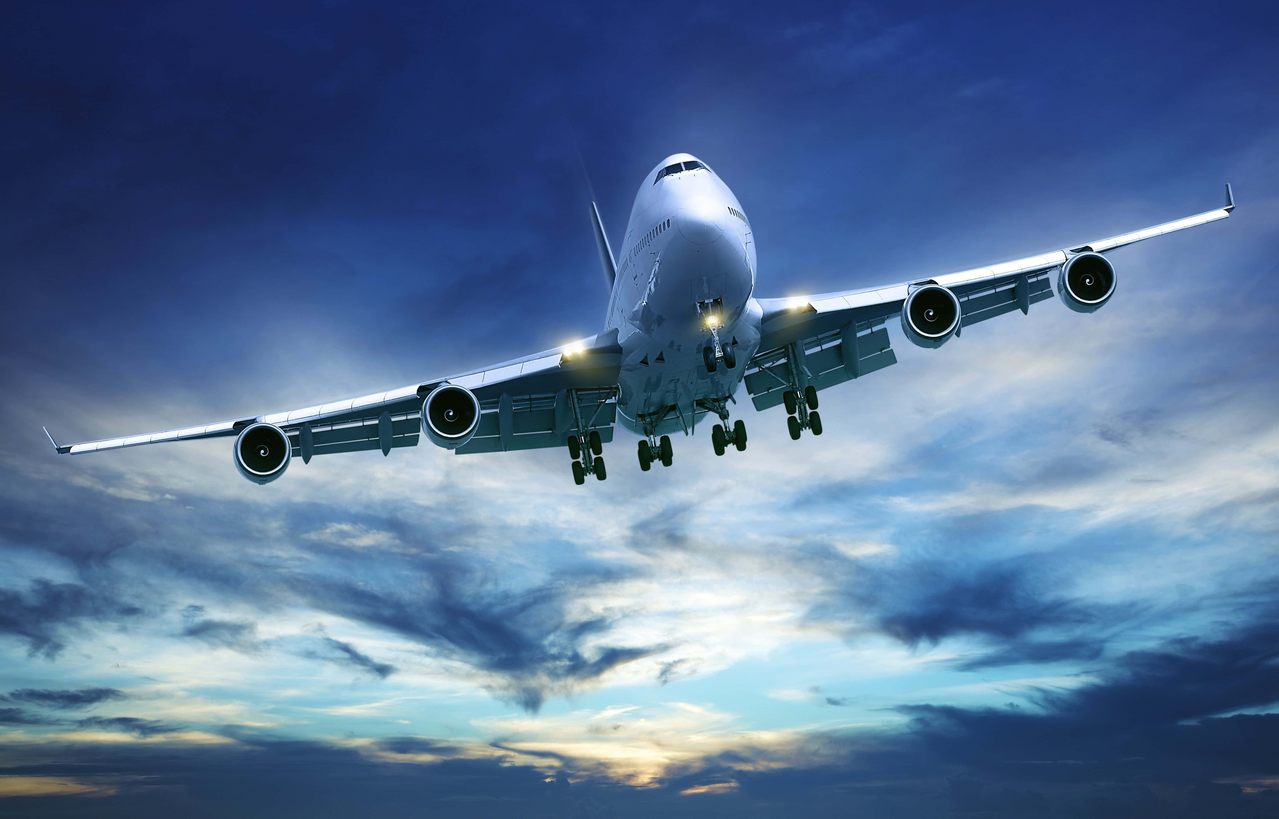 4K 飛機壁紙 桌布 壁紙 — 一架巨大的白色珍寶客機在戲劇性的暮色天空下，放下起落架向地面降落。