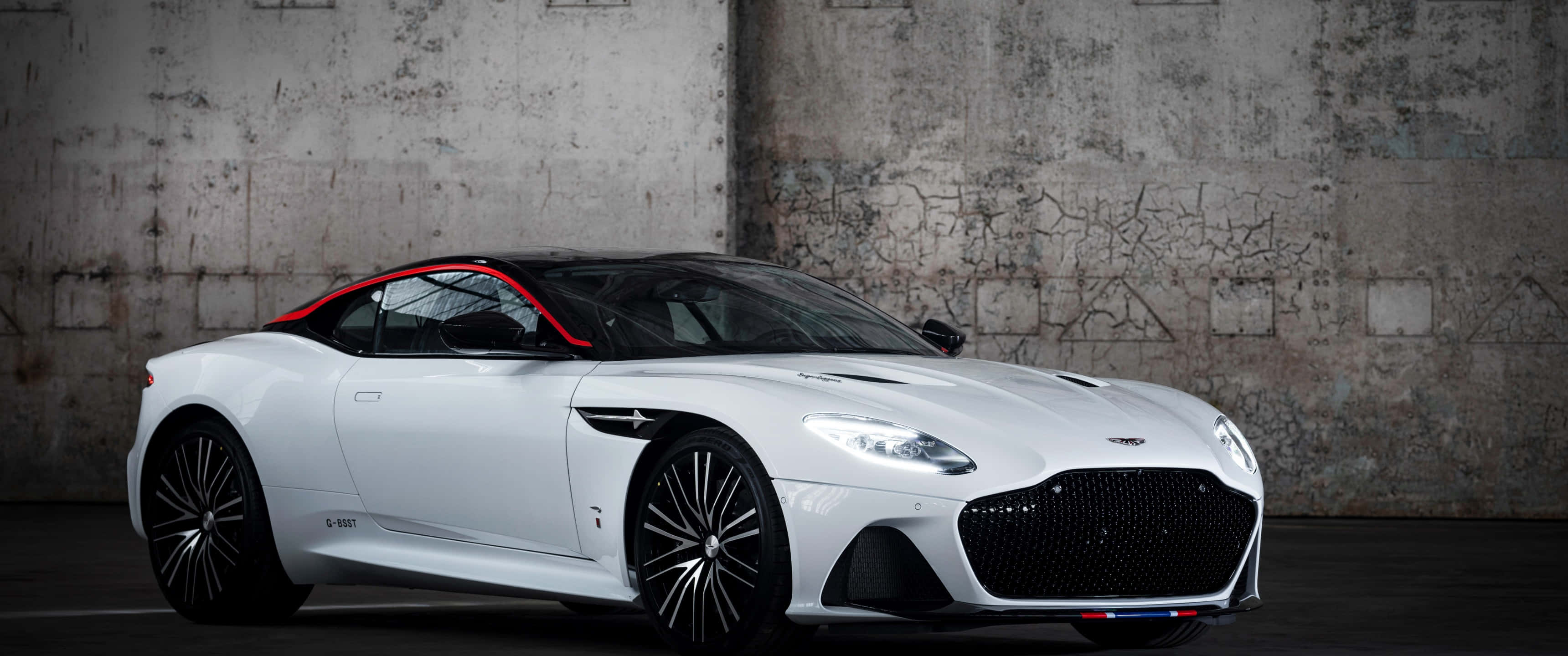 Aston Martin Dbs Superleggera 桌布 壁紙 — 一架帶有紅色點綴的流線型白色Aston Martin DBS Superleggera，停泊在風化的混凝土牆前。