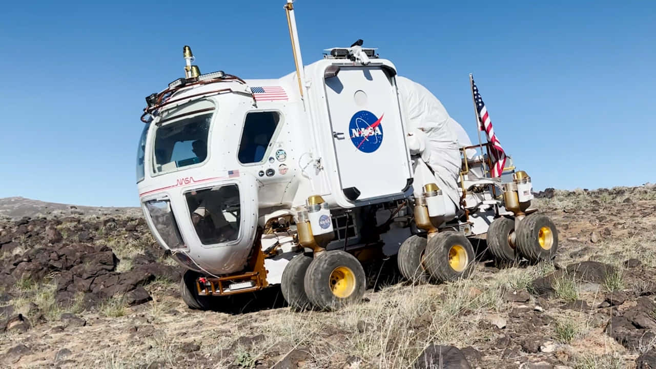 Lunar Rover 桌布 壁紙 — 一架帶有美國國旗的NASA月球車停在岩石沙漠地形上，天空清澈湛藍。