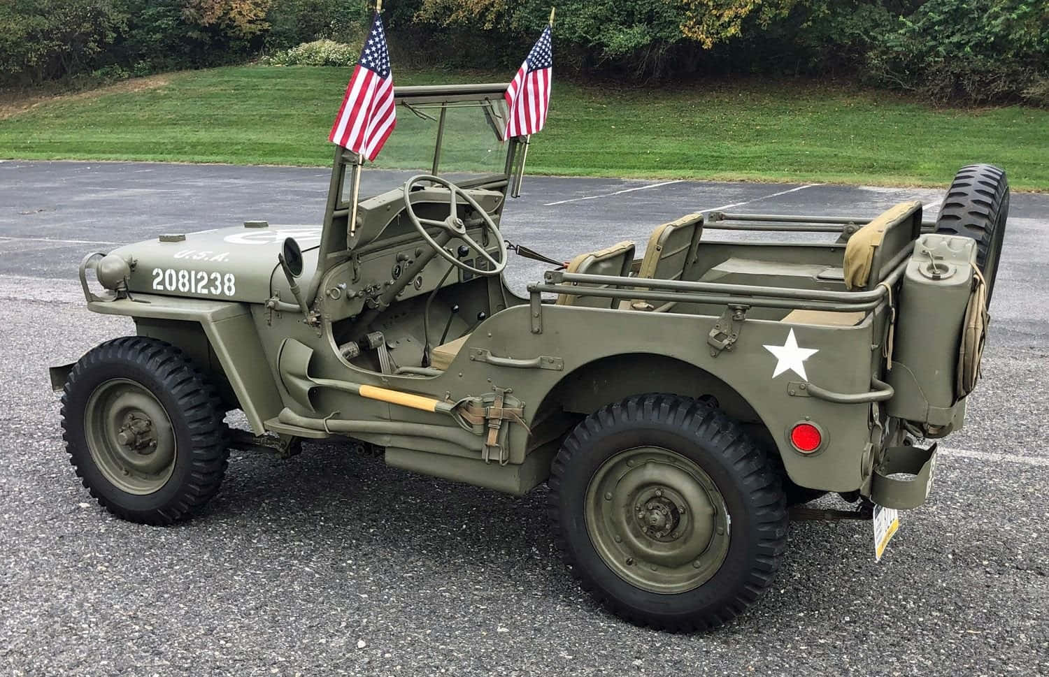 Jeep Willys 桌布 壁紙 — 一架帶有美國國旗的復古橄欖綠軍用吉普車停在碎石地上，周圍是綠草和樹木。