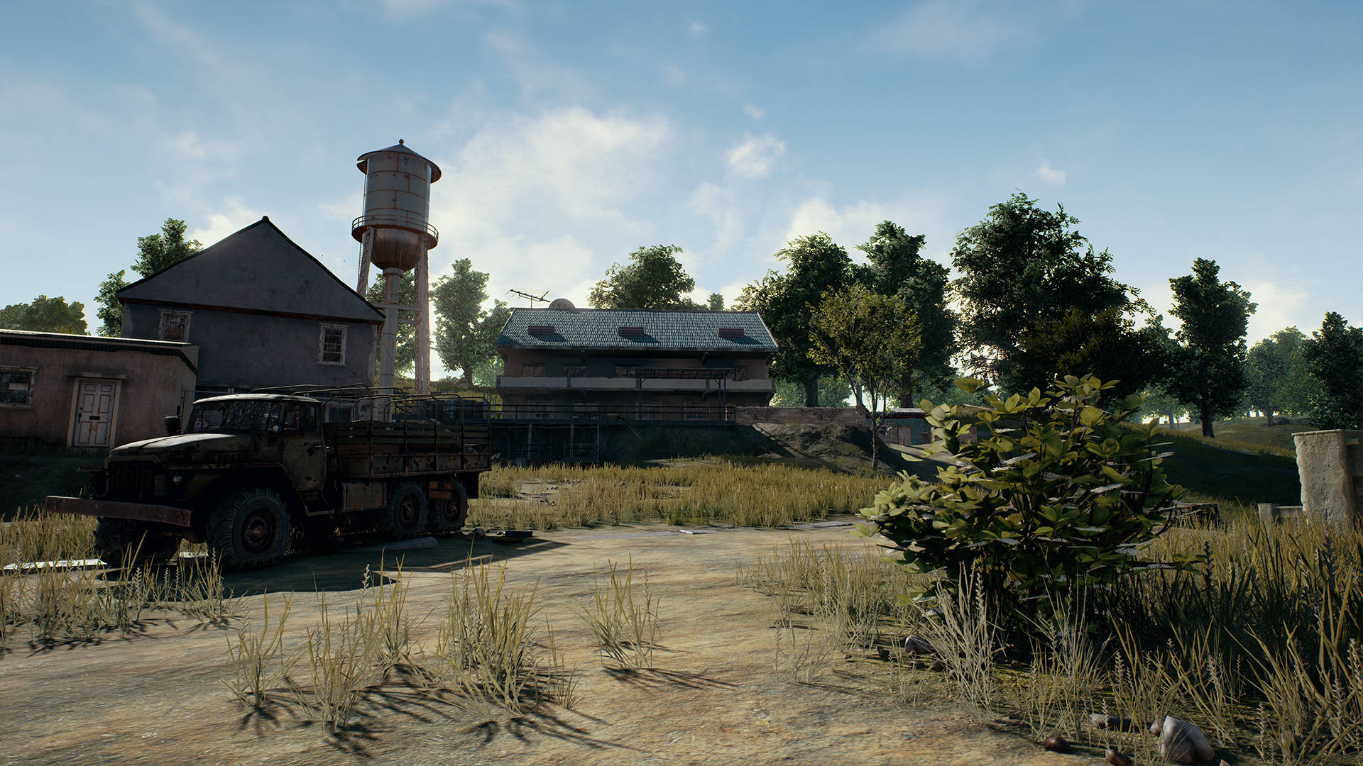 PUBG 桌布 壁紙 — 一架廢棄軍車停喺雜草叢生嘅田野，附近有破舊建築物同水塔，天空晴朗蔚藍。