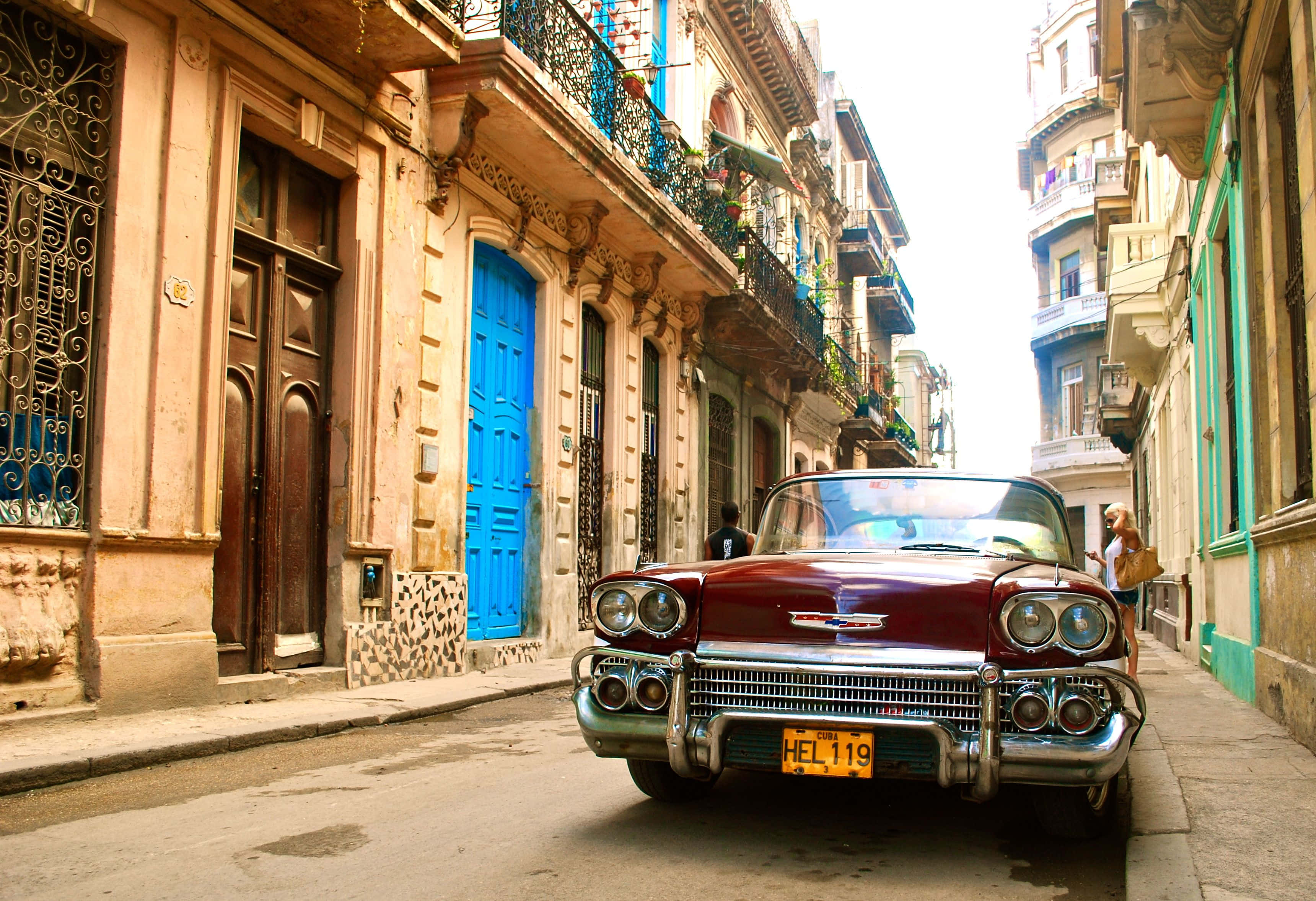 Cuba 桌布 壁紙 — 一架復古紅色開篷車停泊在陽光明媚的哈瓦那街道上，兩旁是色彩繽紛的殖民時期建築和鐵藝陽台。