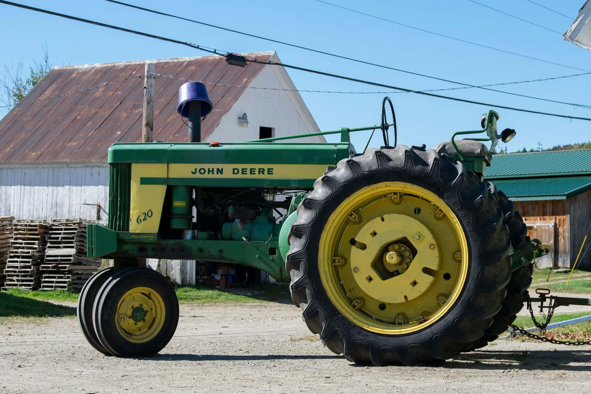John Deere 桌布 壁紙 — 一架復古綠色和黃色的約翰迪爾620拖拉機停泊在碎石路上，前面是風化的穀倉，背景是晴朗的藍天。