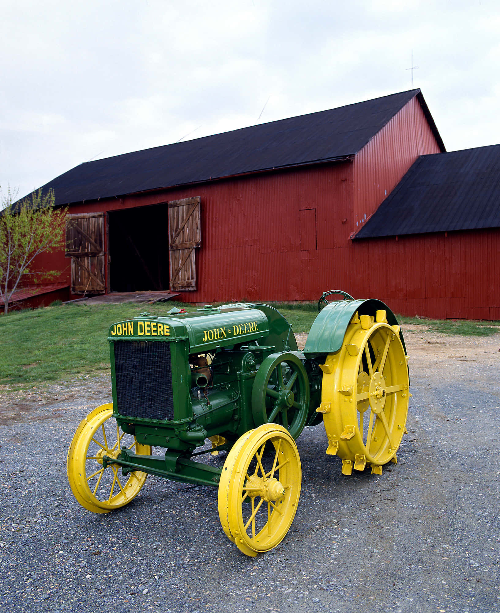 John Deere 桌布 壁紙 — 一架復古綠色和黃色的約翰迪爾拖拉機停在紅色的穀倉前的礫石上，天空多雲。