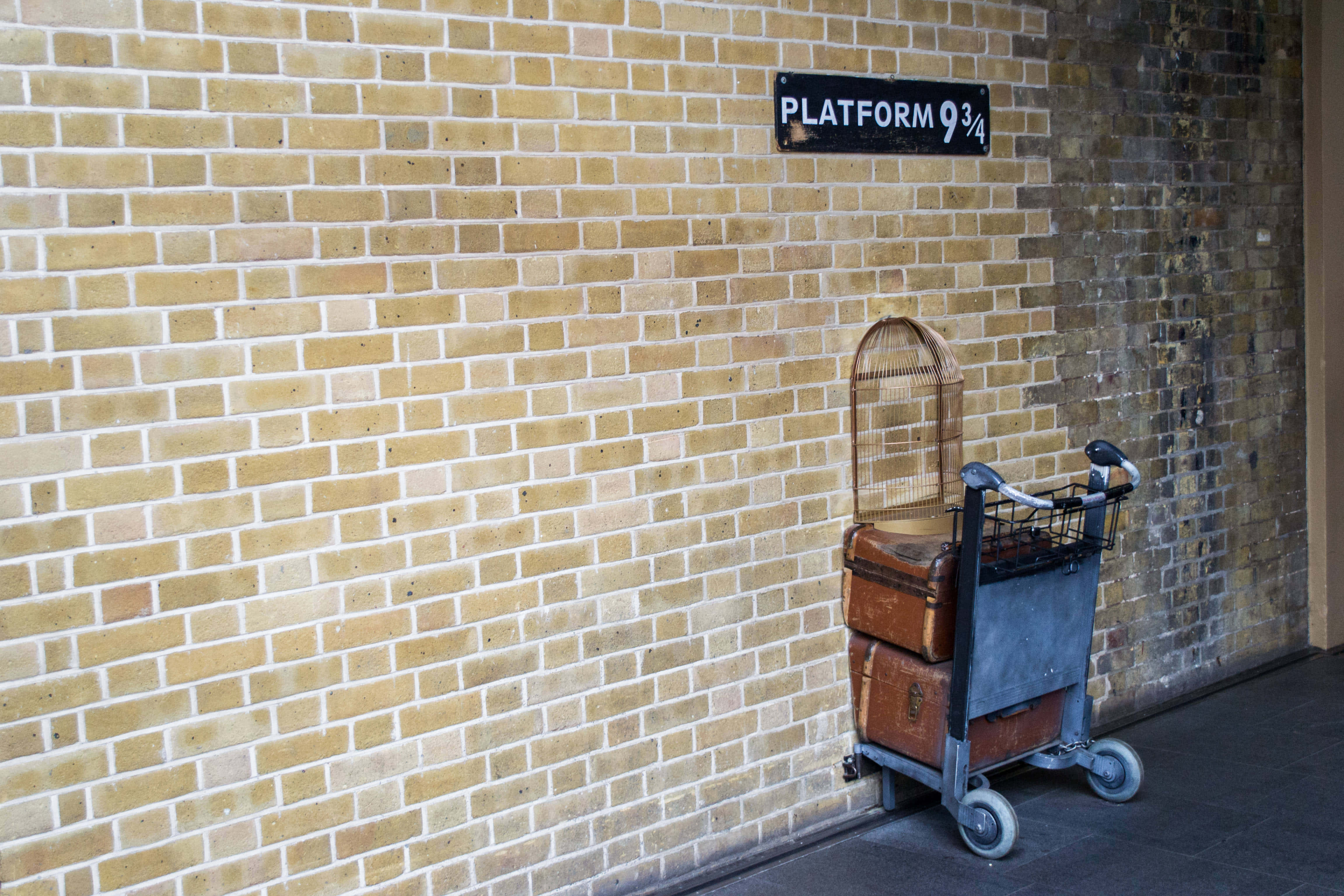Platform 9 3/4 桌布 壁紙 — 一架復古行李車堆滿舊皮箱，佇立在磚牆旁，牆上有『9¾月台』標誌。