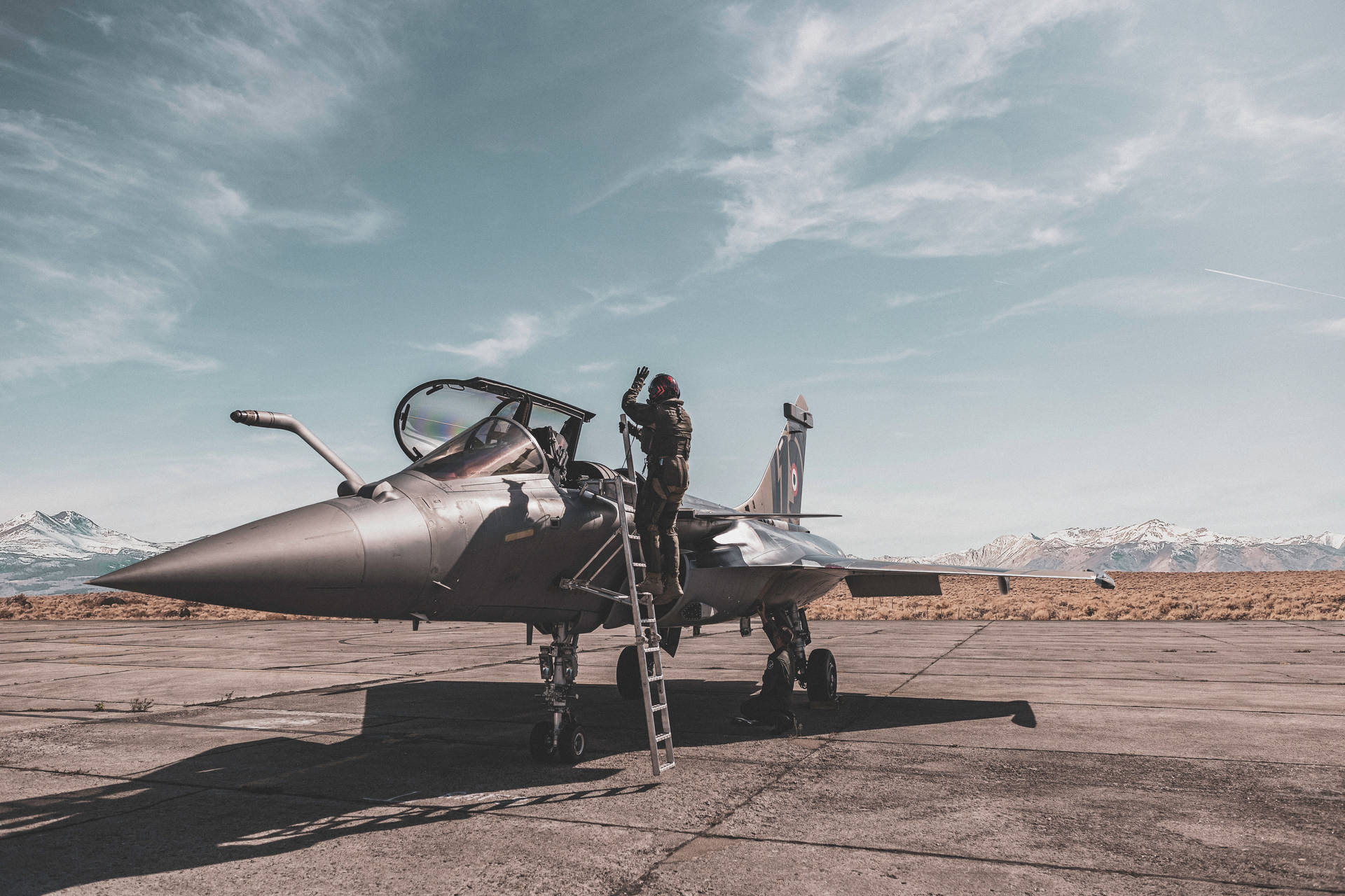 機師在停機坪上攀爬戰鬥機的梯子，背景有雪山。 — 軍事動圖 壁紙