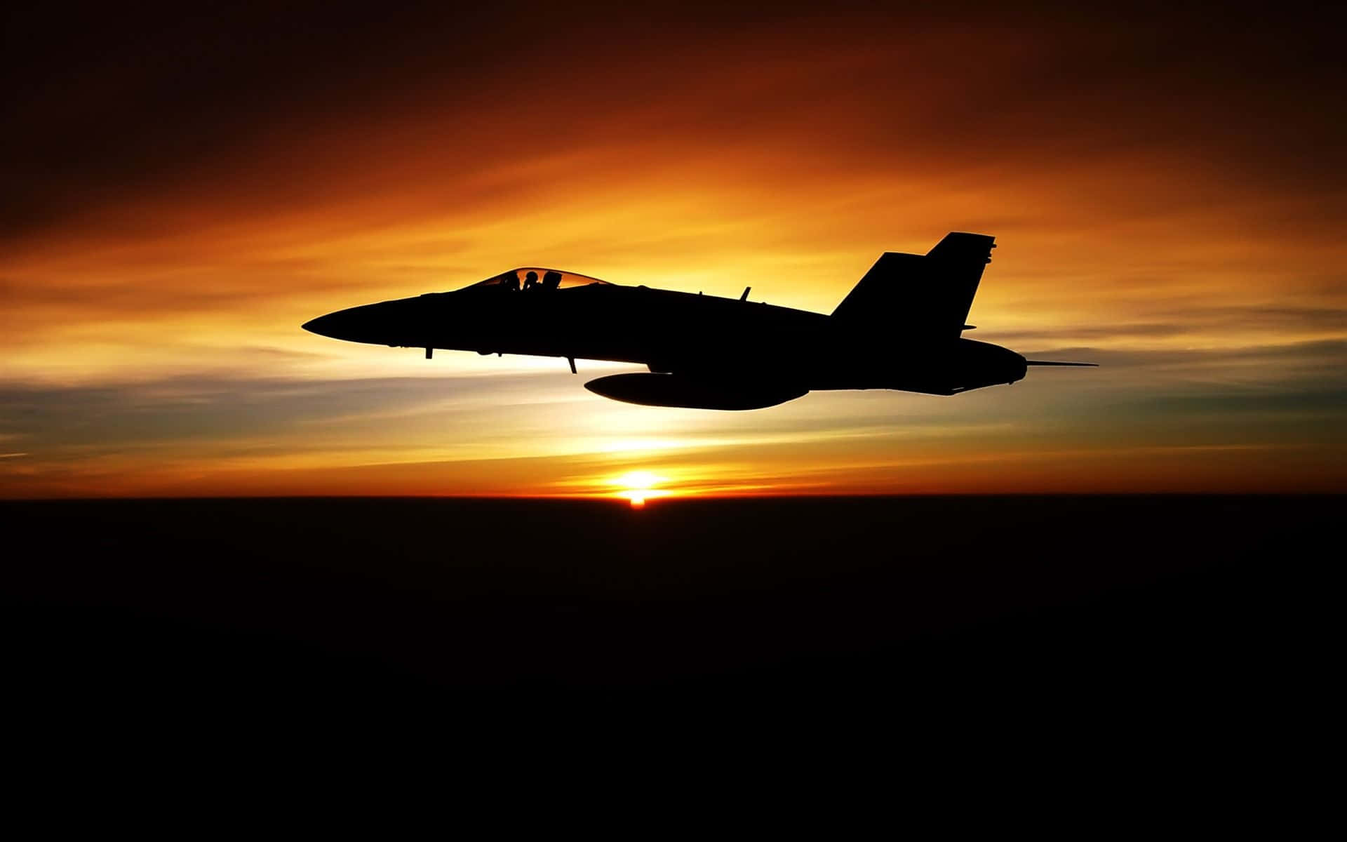 Air Force 桌布 壁紙 — 一架戰鬥機在熾熱的日落天空襯托下，呈現剪影，伴隨著發光的橙色和黃色雲彩。