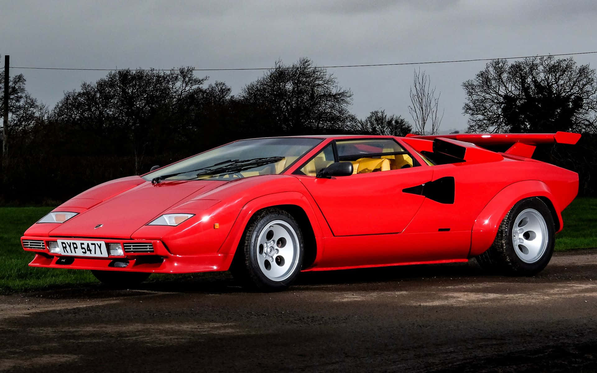 Lamborghini Countach 桌布 壁紙 — 一架搶眼的紅色林寶堅尼Countach跑車停泊在碎石路上，背景是光禿禿的樹木和陰天。