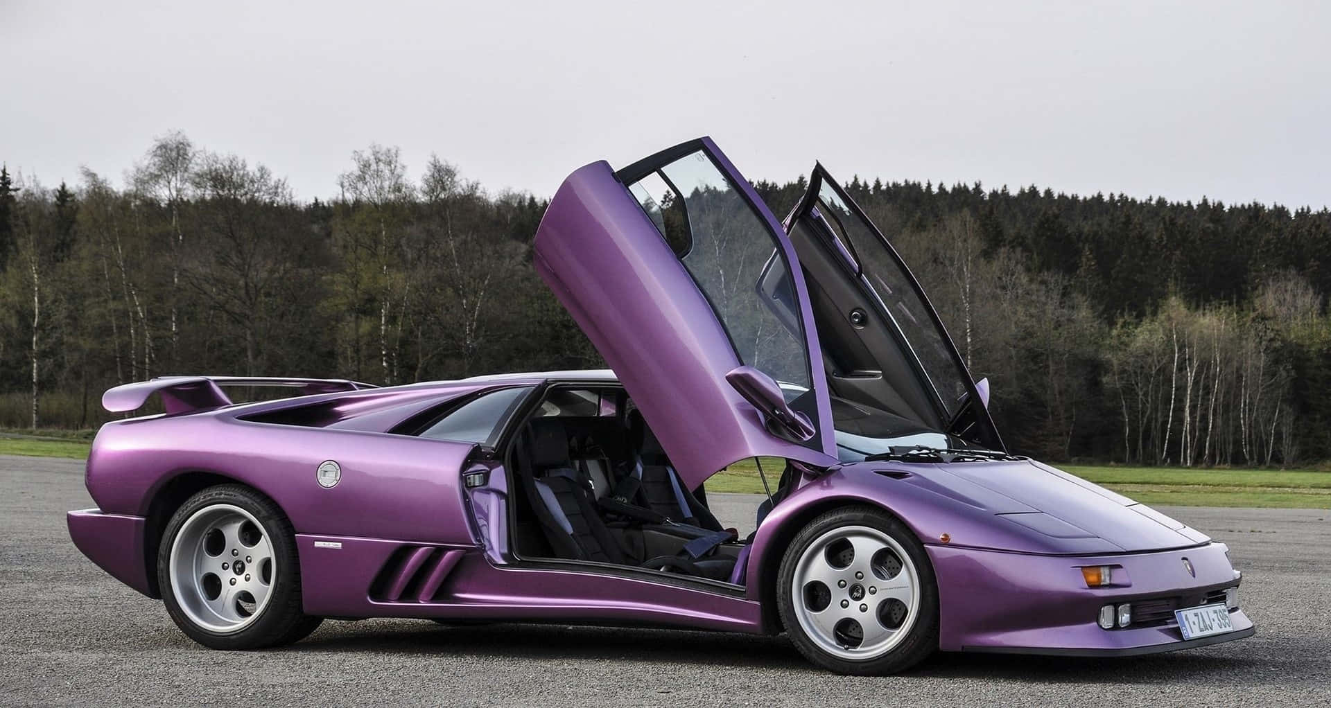 Lamborghini Diablo 桌布 壁紙 — 一架搶眼的紫色林寶堅尼 Diablo 打開鷗翼車門，停泊在森林環繞的瀝青路上。