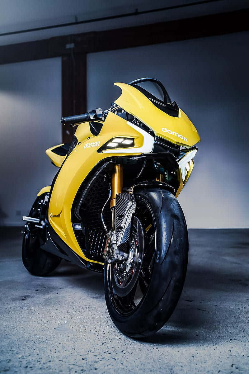 Electric Bike 桌布 壁紙 — 一架搶眼的黃色Damon電單車，配備金色前叉和黑色飾件，在極簡混凝土車庫中，於戲劇性燈光下蓄勢待發。