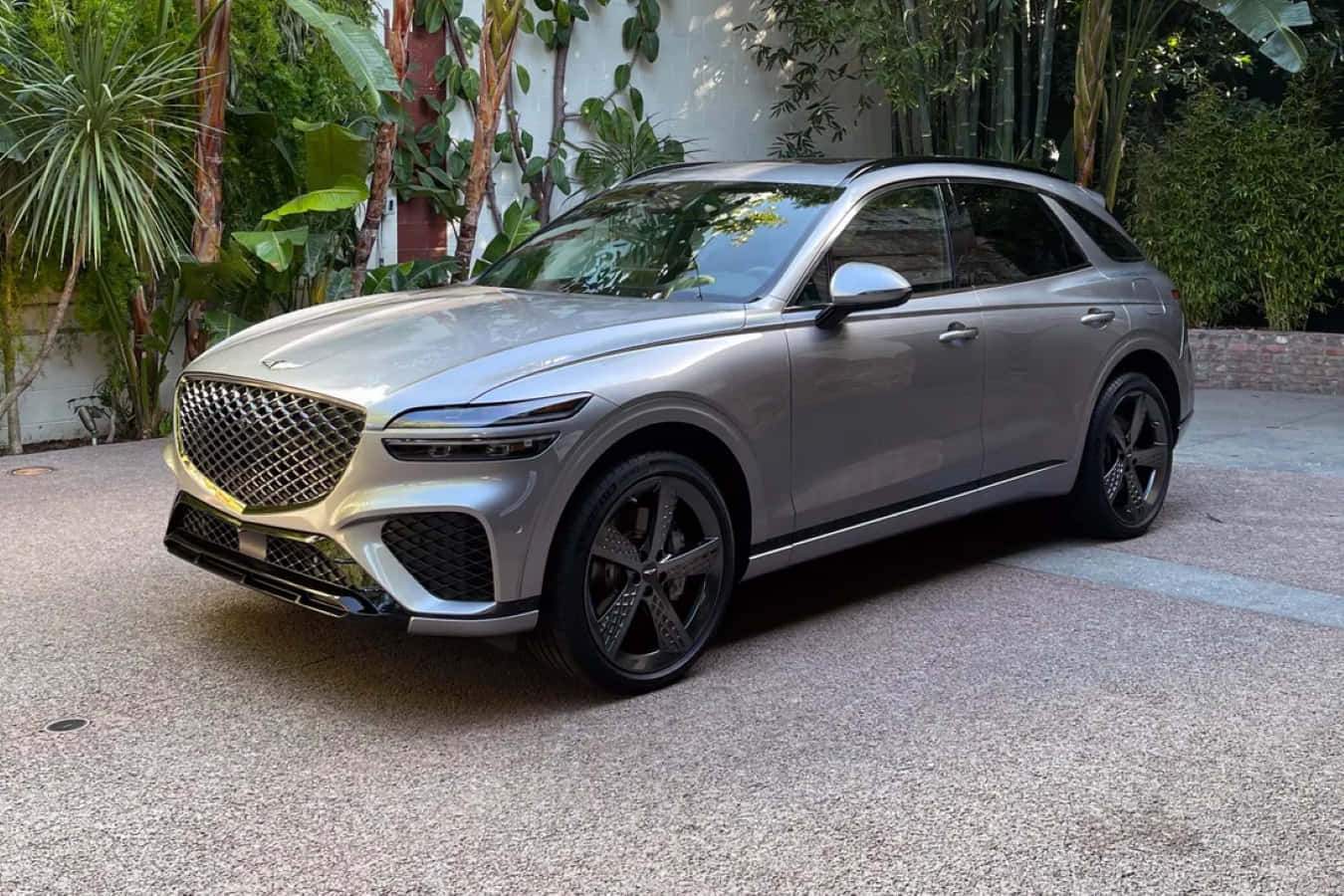 Genesis Gv70 桌布 壁紙 — 一架時尚嘅銀色 Genesis GV70 SUV 泊喺被茂盛熱帶植物圍繞嘅混凝土車道上。