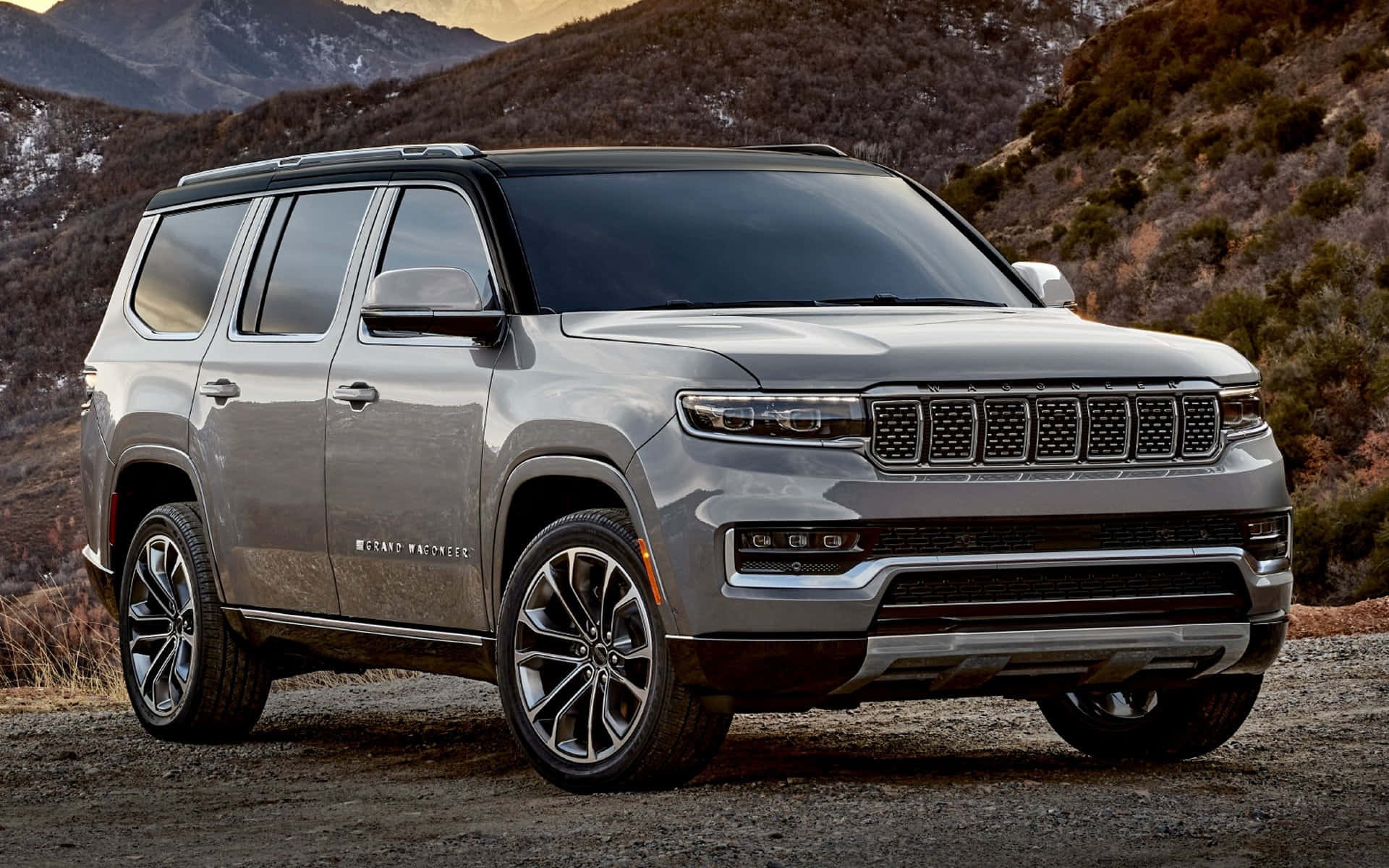 Jeep Wagoneer 桌布 壁紙 — 一架時尚嘅銀色Jeep Grand Wagoneer SUV泊喺碎石路上，背景係崎嶇嘅山脈。