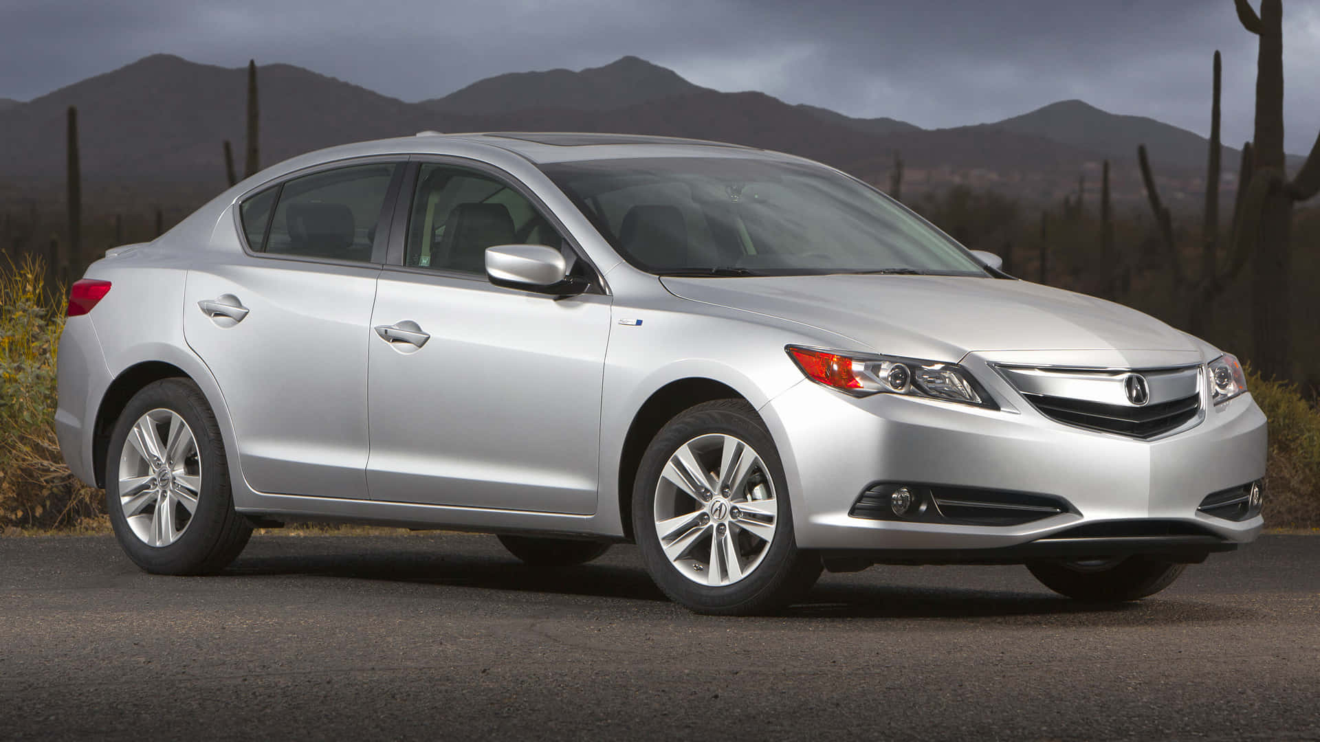 Acura Ilx 桌布 壁紙 — 一架時尚嘅銀色房車停泊喺瀝青路上，背景係山脈同仙人掌，天空多雲。