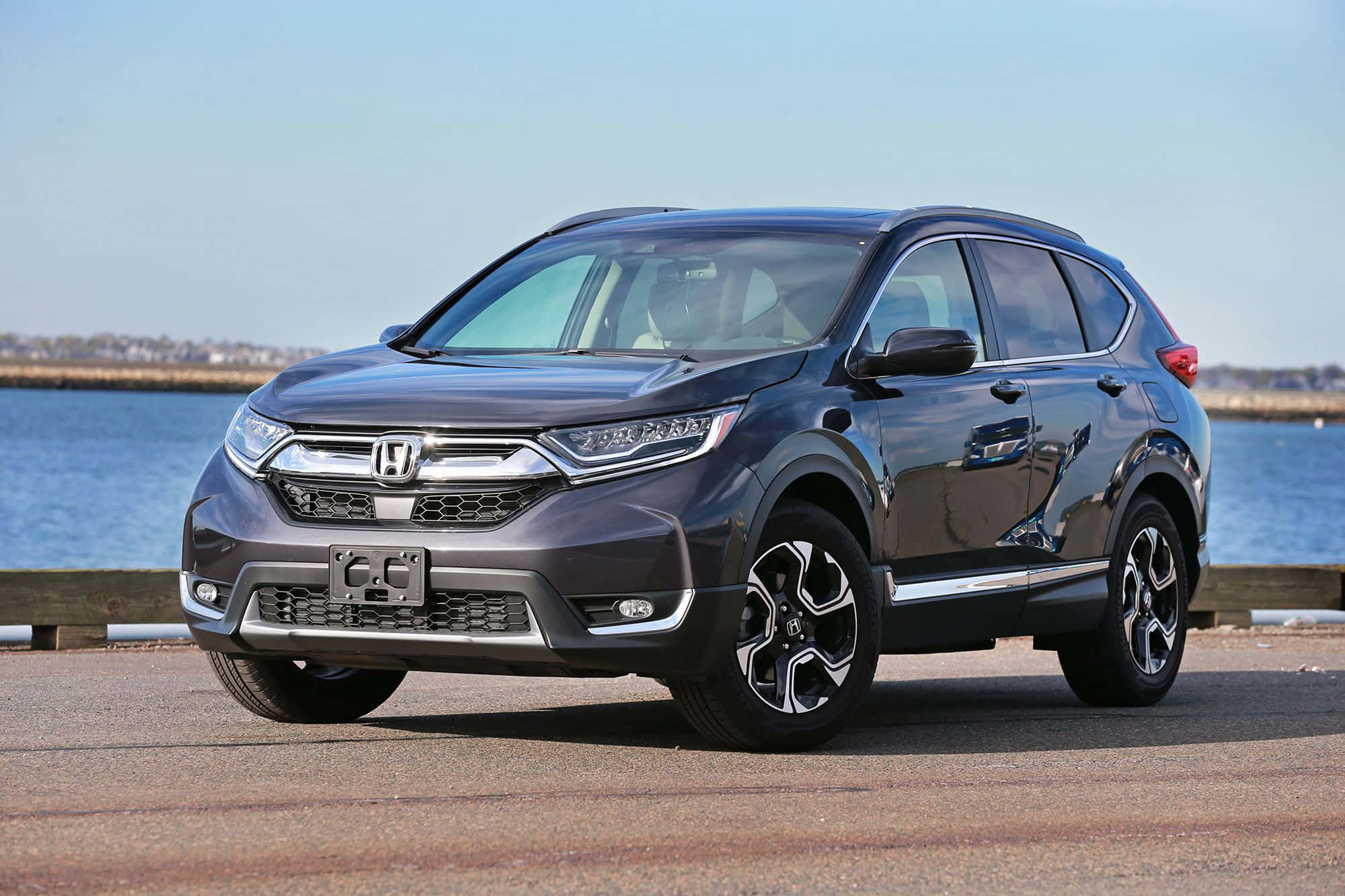 Honda Cr-v 桌布 壁紙 — 一架時尚深灰色本田CR-V SUV停泊在海濱，平靜的藍色海水和遠處的海岸線，天空晴朗。