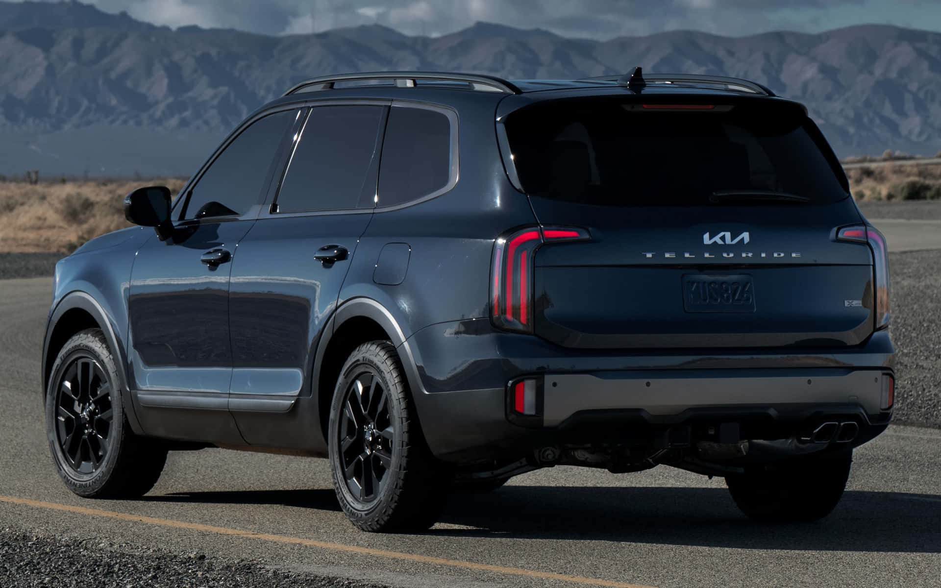 Kia Telluride 桌布 壁紙 — 一架時尚深藍色Kia Telluride SUV停泊在沙漠公路上，背景是崎嶇的山脈，天空晴朗。