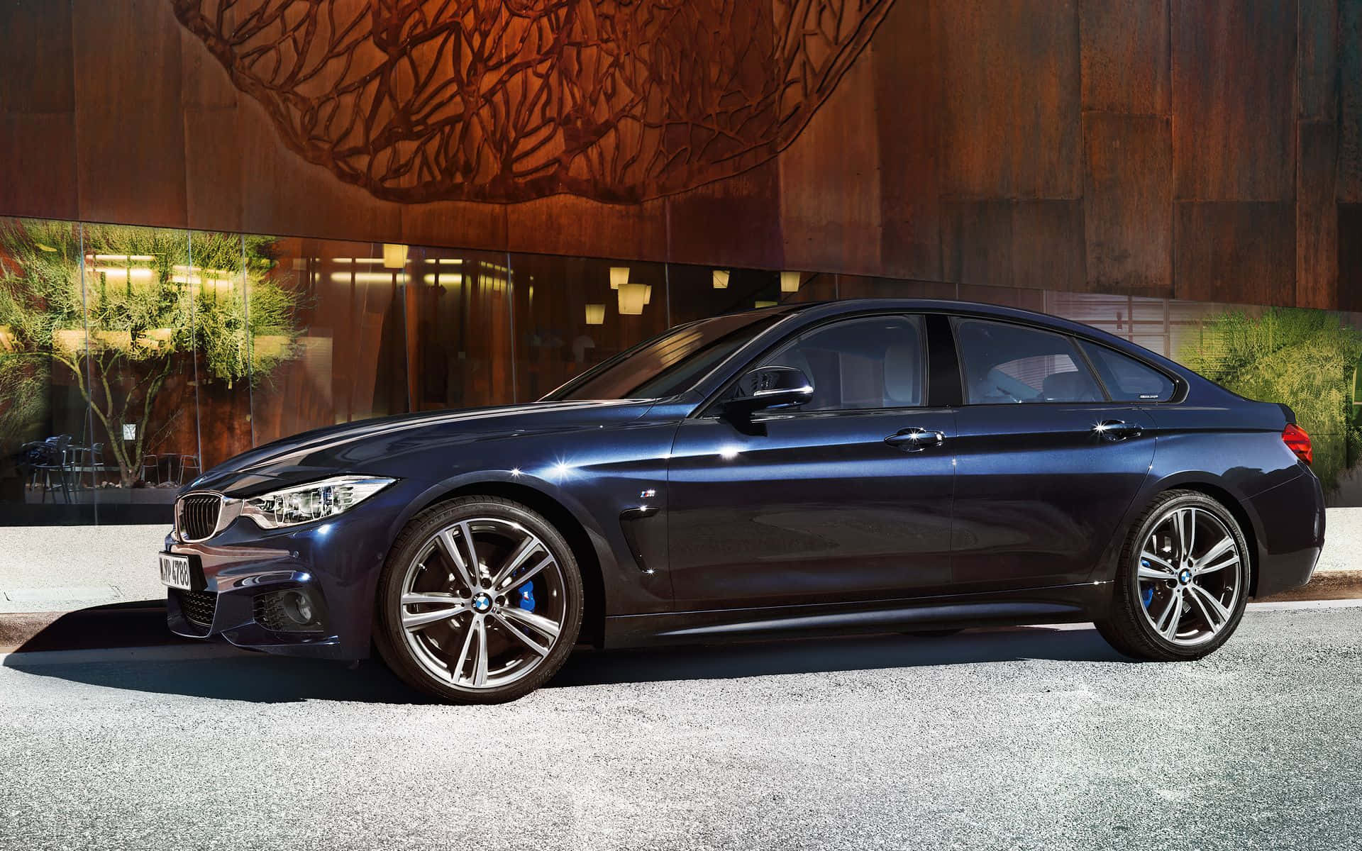 Bmw 4 Series 桌布 壁紙 — 一架時尚深藍色寶馬房車停泊在碎石路上，前方是現代建築，外牆為木質並配以玻璃窗。