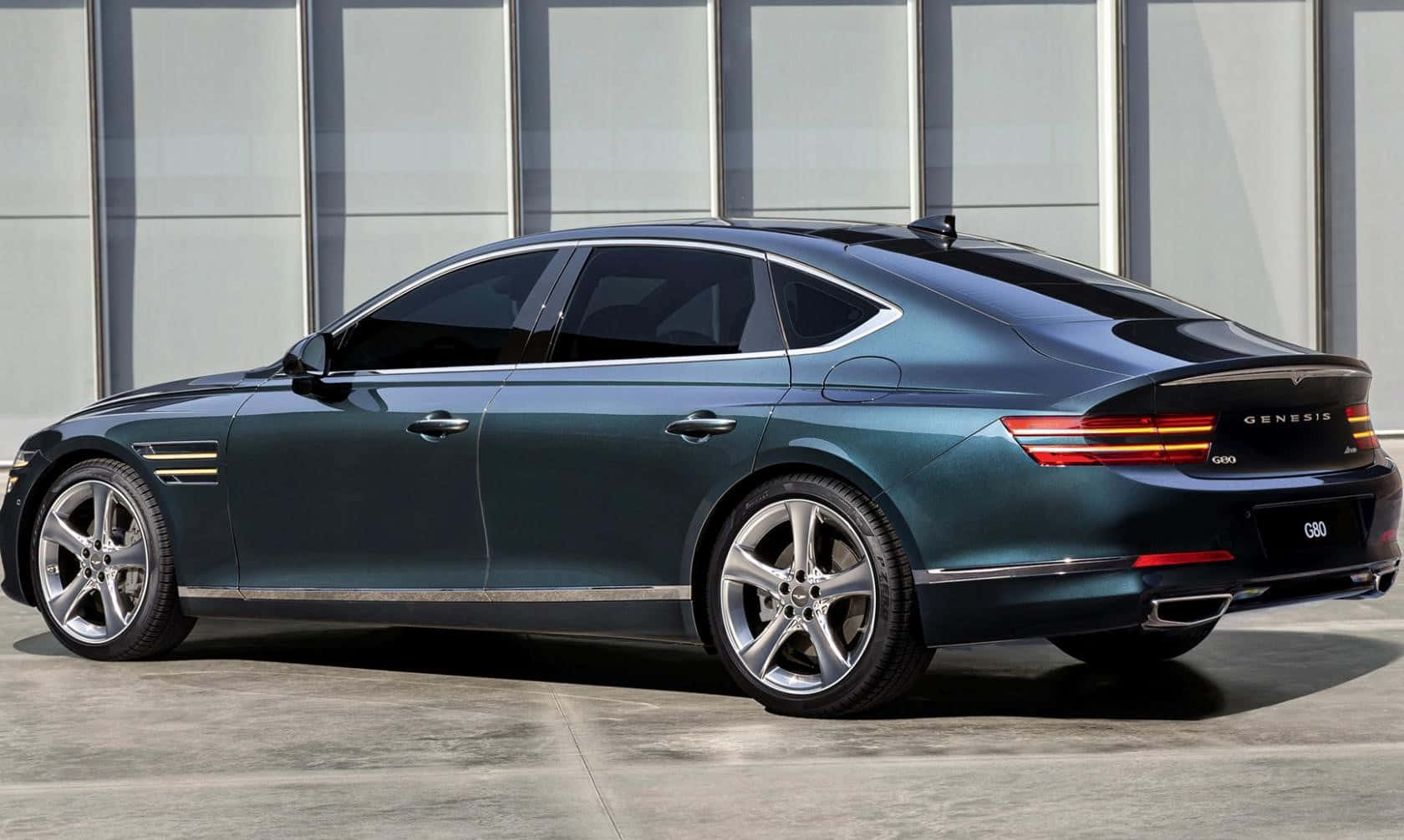Genesis G80 桌布 壁紙 — 一架時尚深青綠色Genesis G90豪華房車停在混凝土上，以現代玻璃建築為背景。