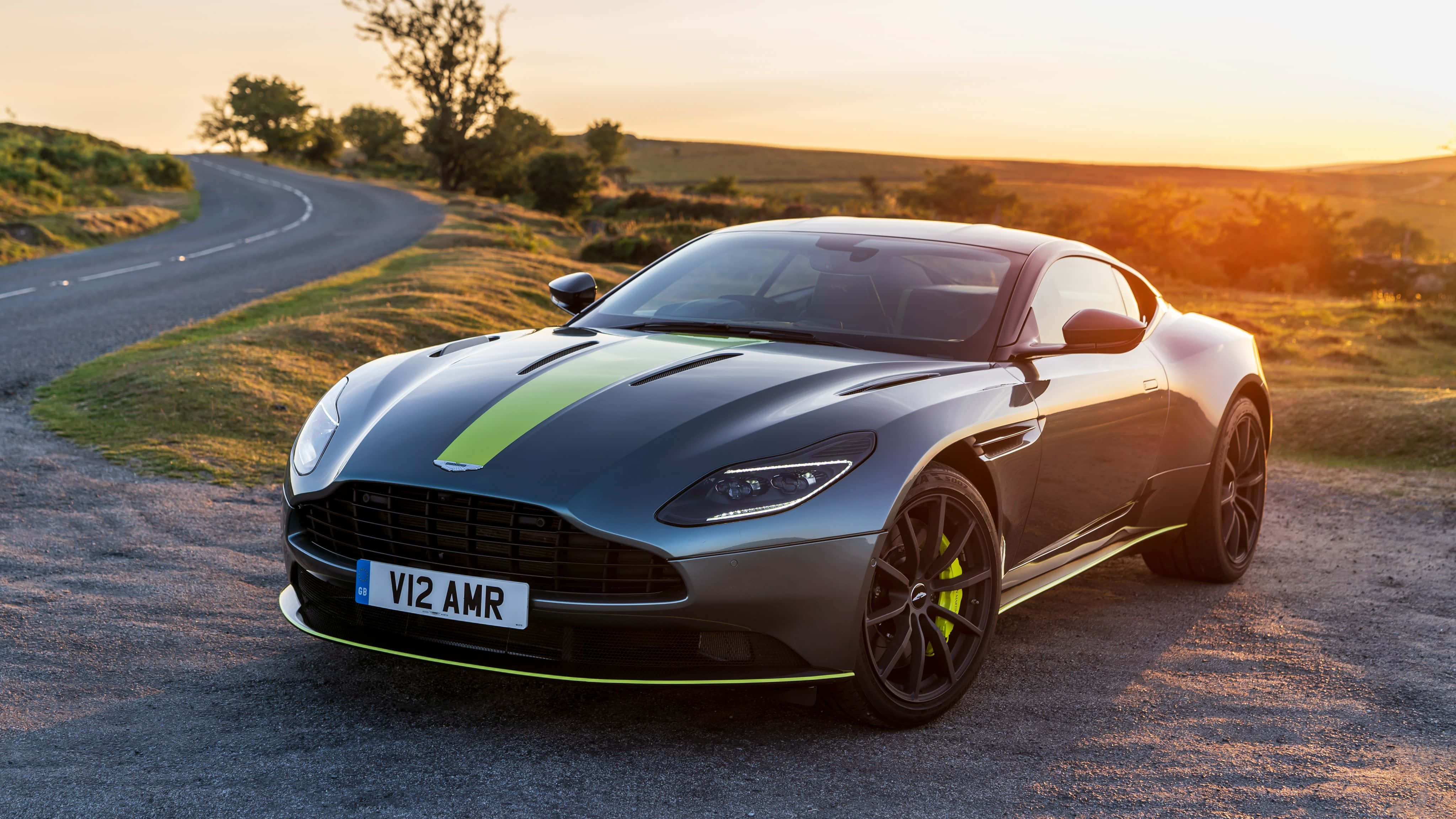 Aston Martin Db11 桌布 壁紙 — 一架時尚灰色 Aston Martin V12 AMR 配以青檸綠色點綴，停泊在金色日落時分的蜿蜒鄉村道路上。