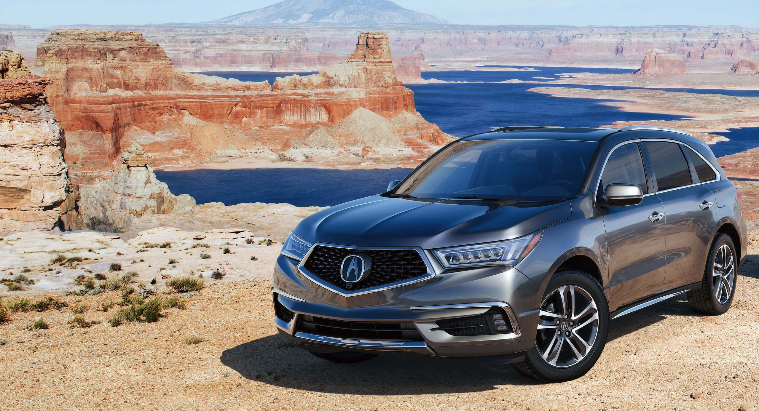 Acura Mdx 桌布 壁紙 — 一架時尚灰色Acura SUV停泊在沙漠地形上，背景有紅色岩石形成和藍色湖泊，天空晴朗。