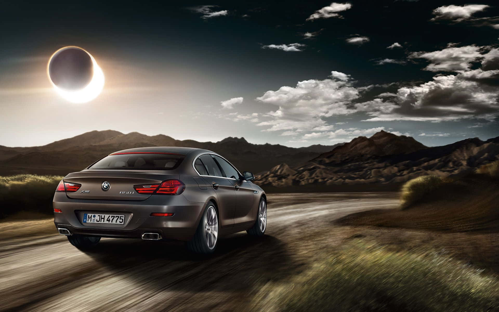 Bmw 6 Series 桌布 壁紙 — 一架時尚灰色BMW 6系在沙漠公路上行駛，背景是戲劇性的日食和崎嶇的山脈。