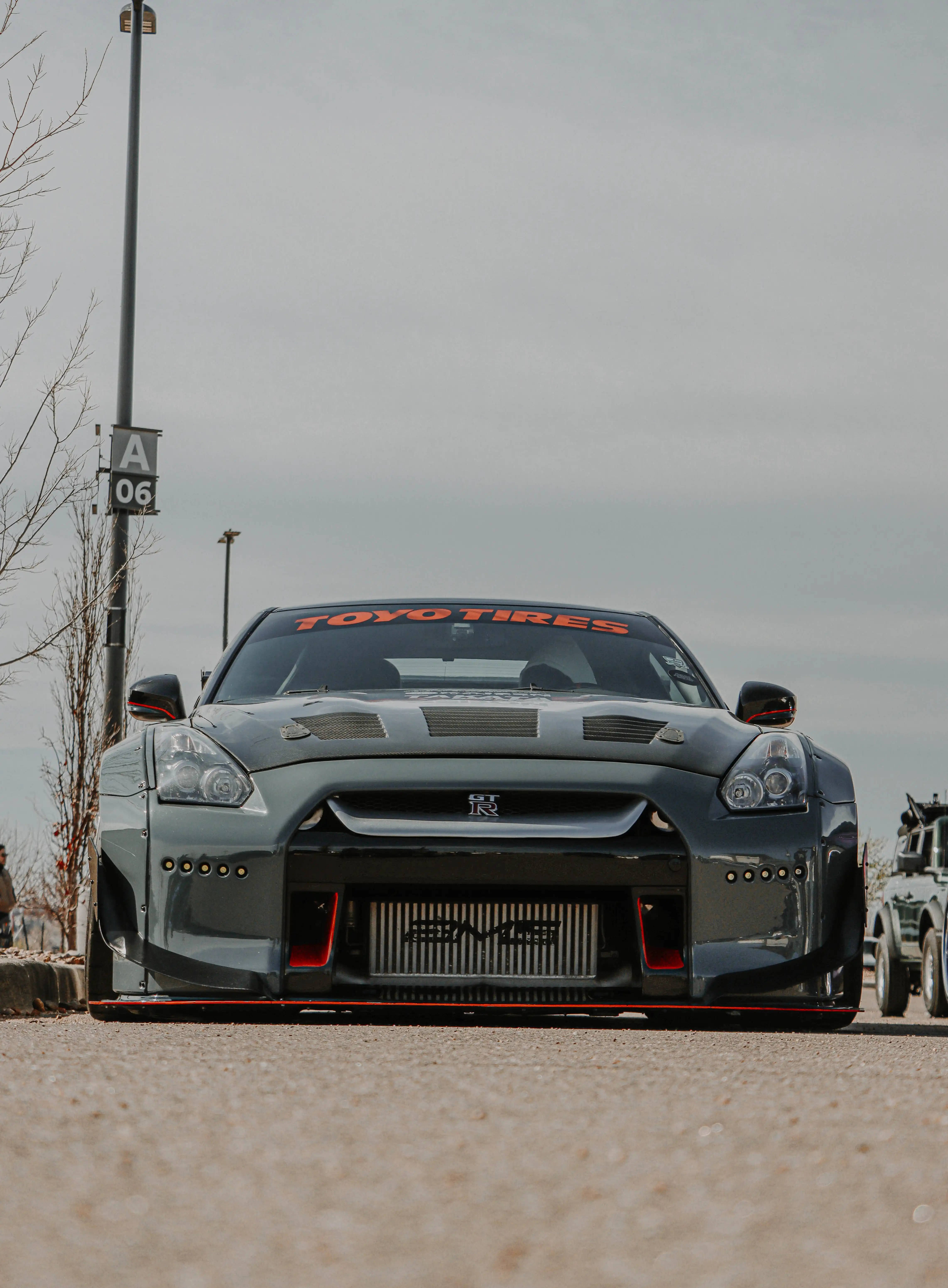 Nissan 桌布 壁紙 — 一架時尚灰色日產GT-R賽車，帶有紅色點綴和Toyo Tires品牌，停泊在陰天下的瀝青路面上。
