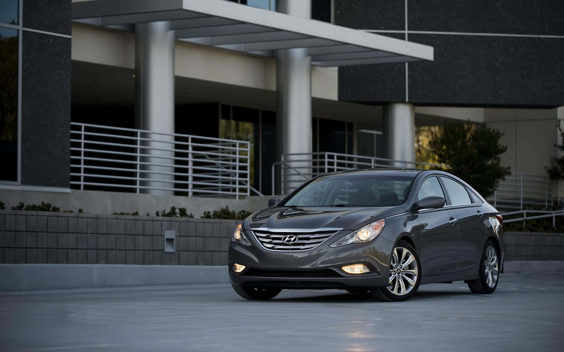 Hyundai Sonata 桌布 壁紙 — 一架時尚灰色現代房車停喺現代建築前面，車頭燈亮起。