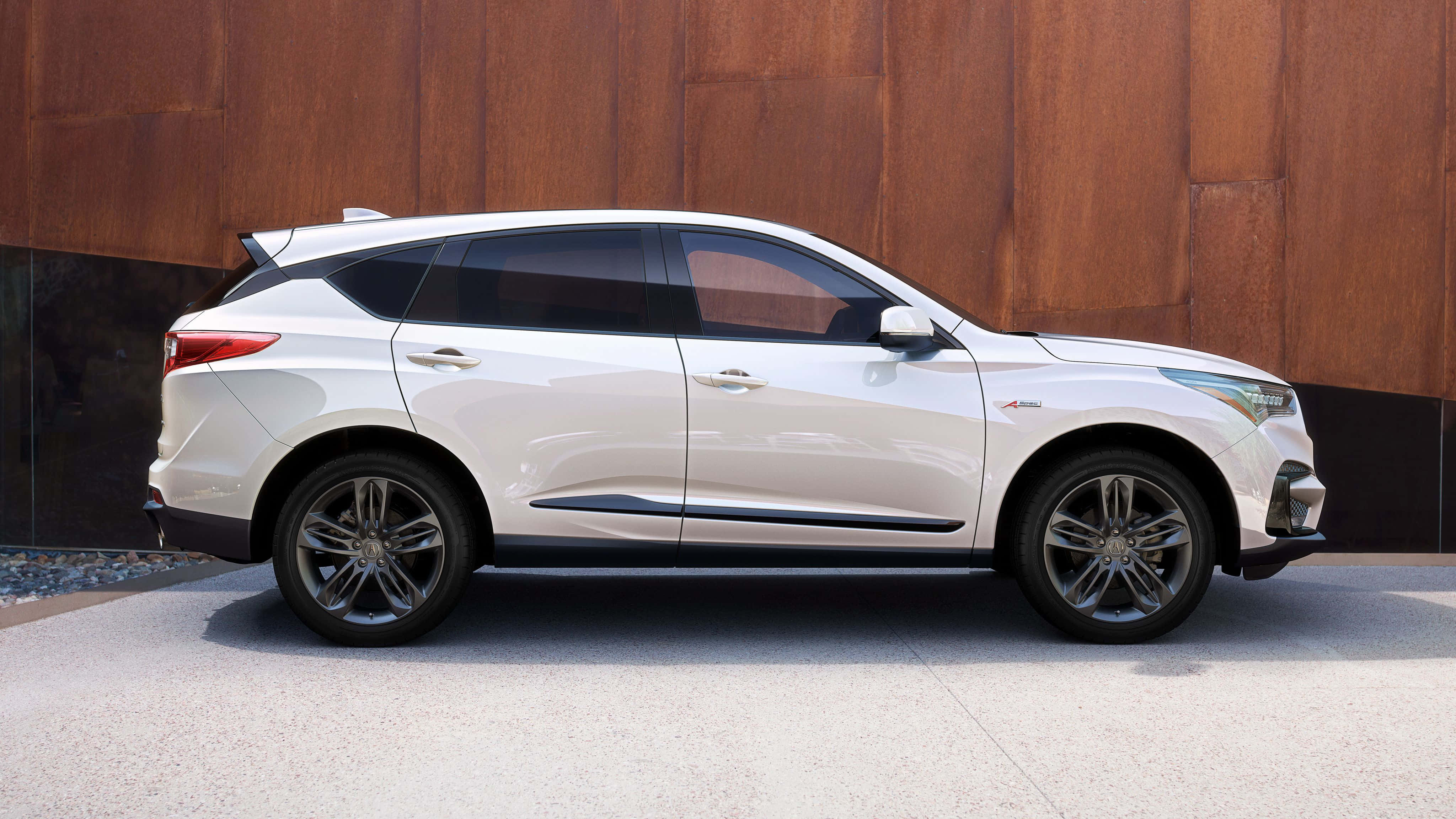 Acura Rdx 桌布 壁紙 — 一架時尚白色SUV在明亮日光下停泊在帶紋理的鏽色牆邊。