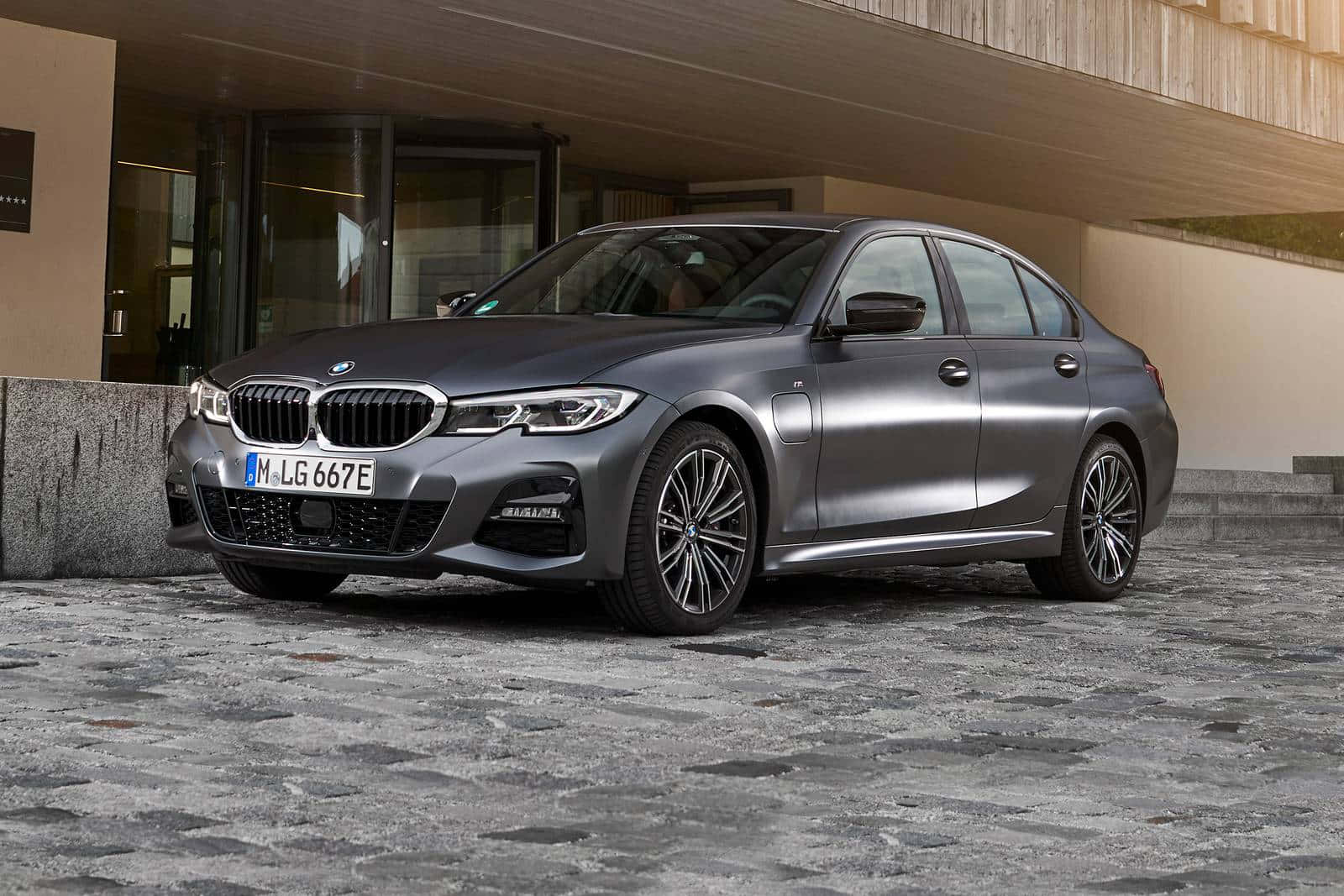 Bmw 3 Series 桌布 壁紙 — 一架時尚的啞光灰色BMW 3系電動轎車停泊在現代建築下的石砌車道上。