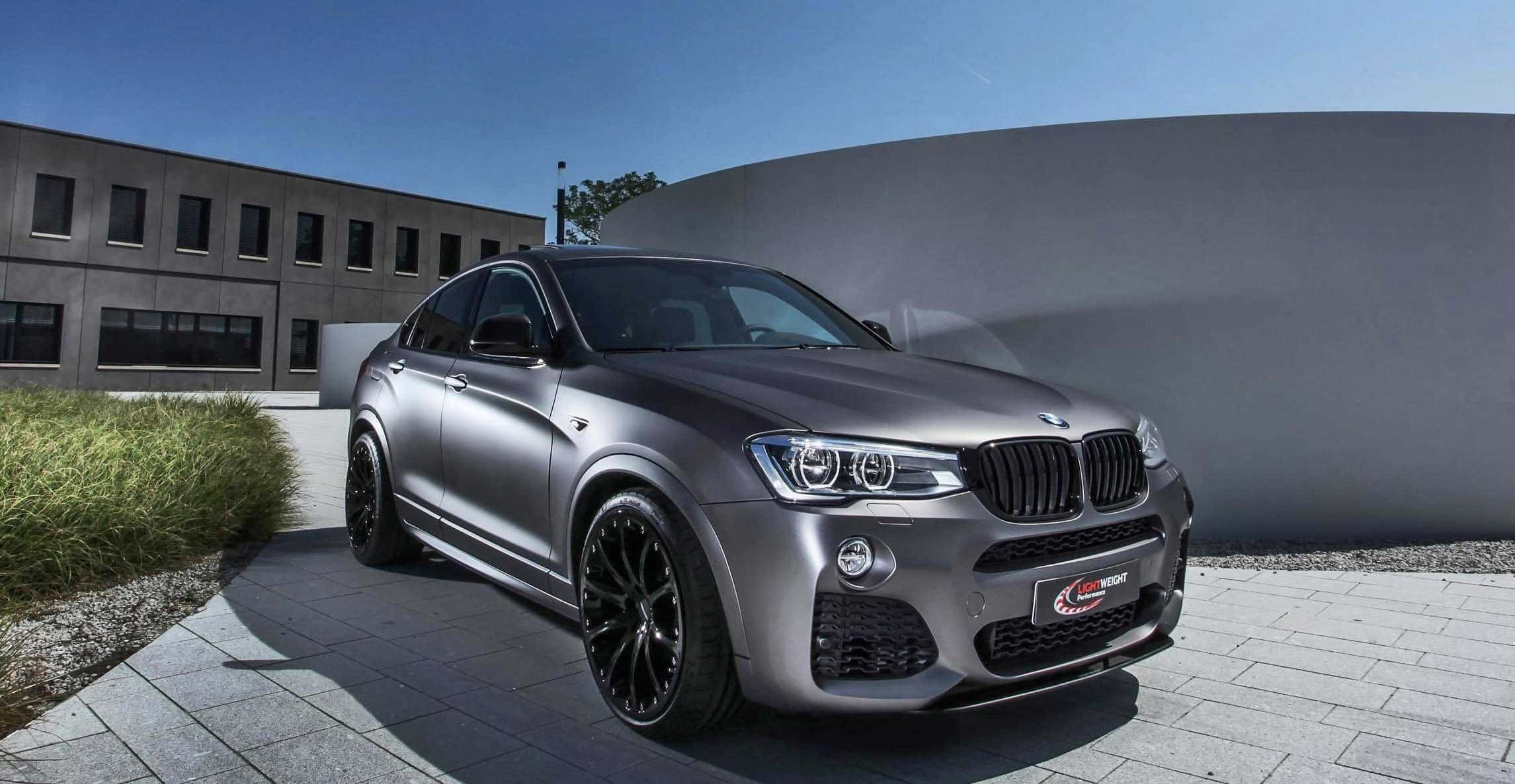 Bmw X4 桌布 壁紙 — 一架時尚的啞光灰色BMW X6M跑車停泊在鋪設瓷磚的庭院中，周圍有現代建築和綠植，頭頂是清澈的藍天。
