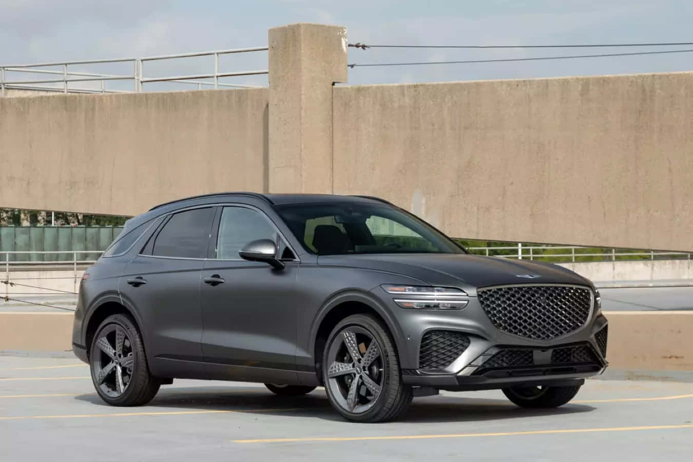 Genesis Gv70 桌布 壁紙 — 一架時尚的啞光灰色SUV停泊在混凝土停車場，周圍是工業風格的牆壁和欄杆，在明亮的日光下。