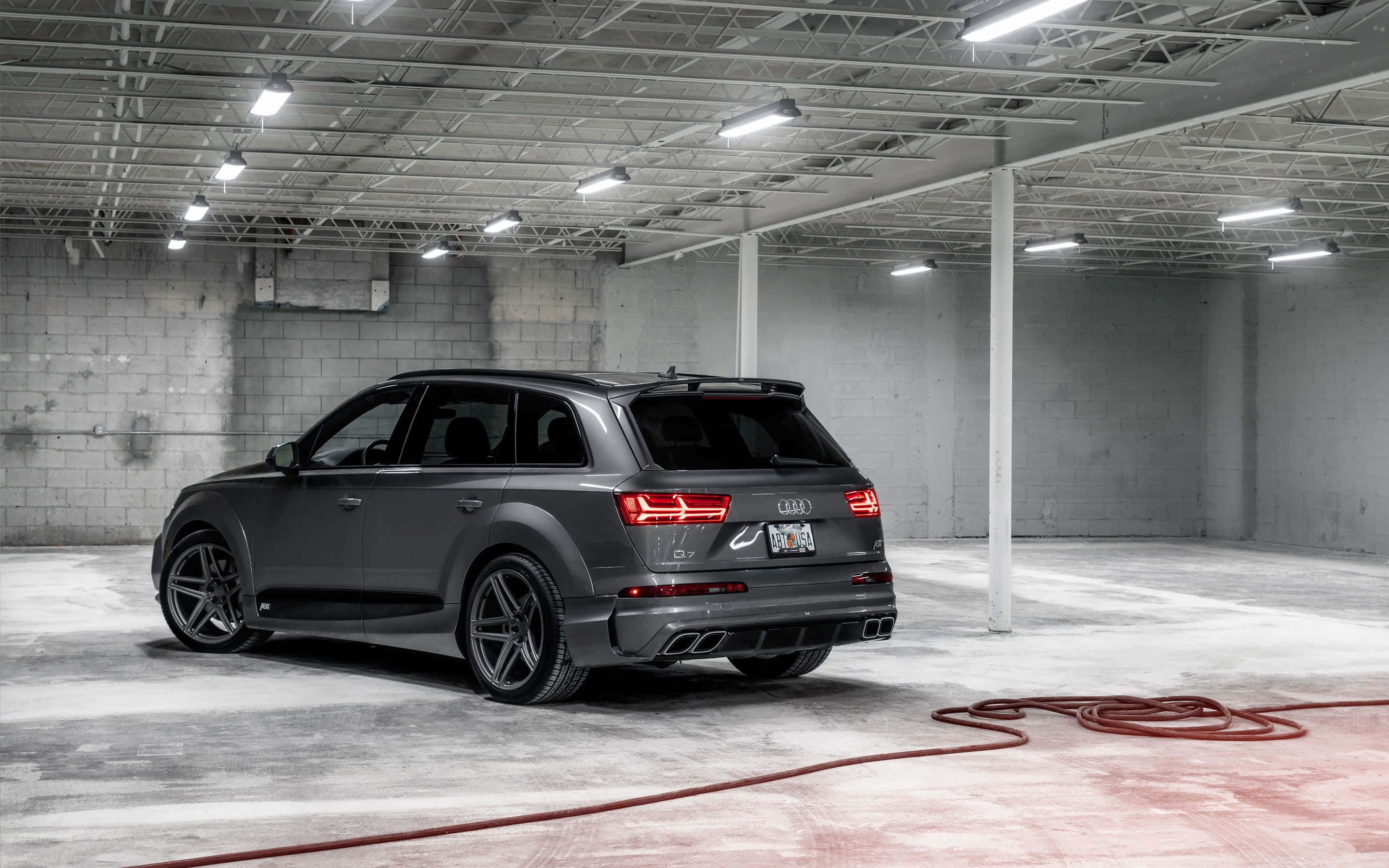 Audi Q7 桌布 壁紙 — 一架時尚的啞光灰色奧迪 SQ7 SUV 停泊在簡約工業風車庫，車庫有外露天花橫樑和混凝土牆。