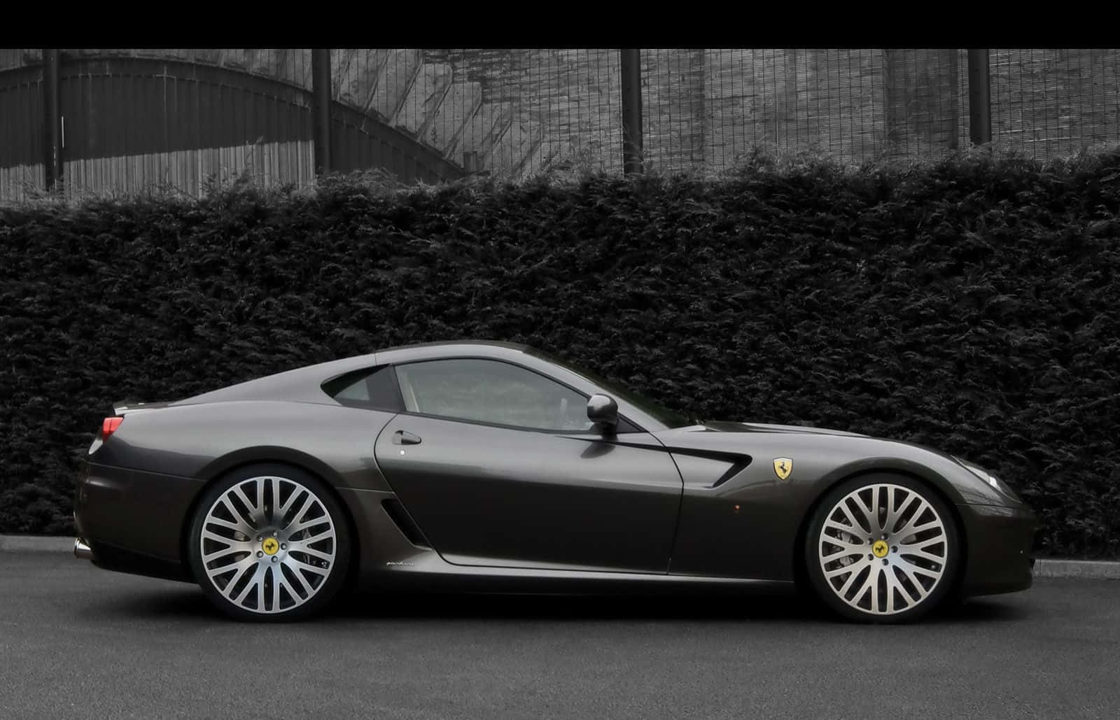 Ferrari 599 Gtb Fiorano 桌布 壁紙 — 一架時尚的啞光灰色法拉利跑車停泊在茂密樹籬旁，在柔和日光下。