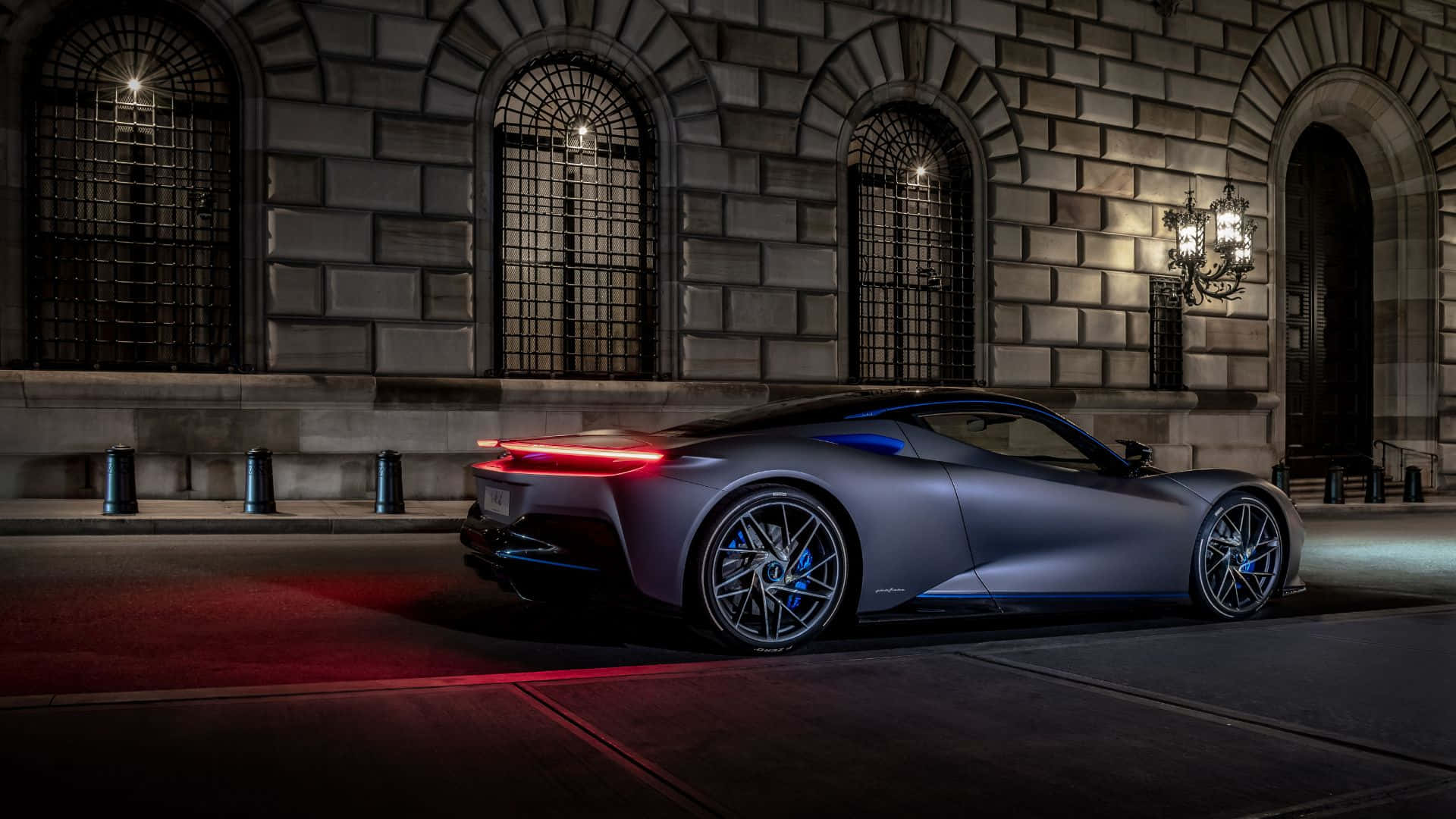 Pininfarina 桌布 壁紙 — 一架時尚的啞光灰色跑車在夜間停在一棟帶有拱形窗戶的宏偉石建築前，紅色尾燈閃爍。