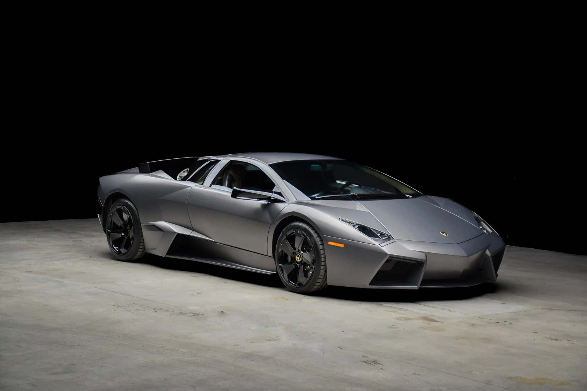 Lamborghini Reventón 桌布 壁紙 — 一架時尚的啞光銀色林寶堅尼Reventon跑車在黑色背景下的混凝土地板上被戲劇性地照亮。