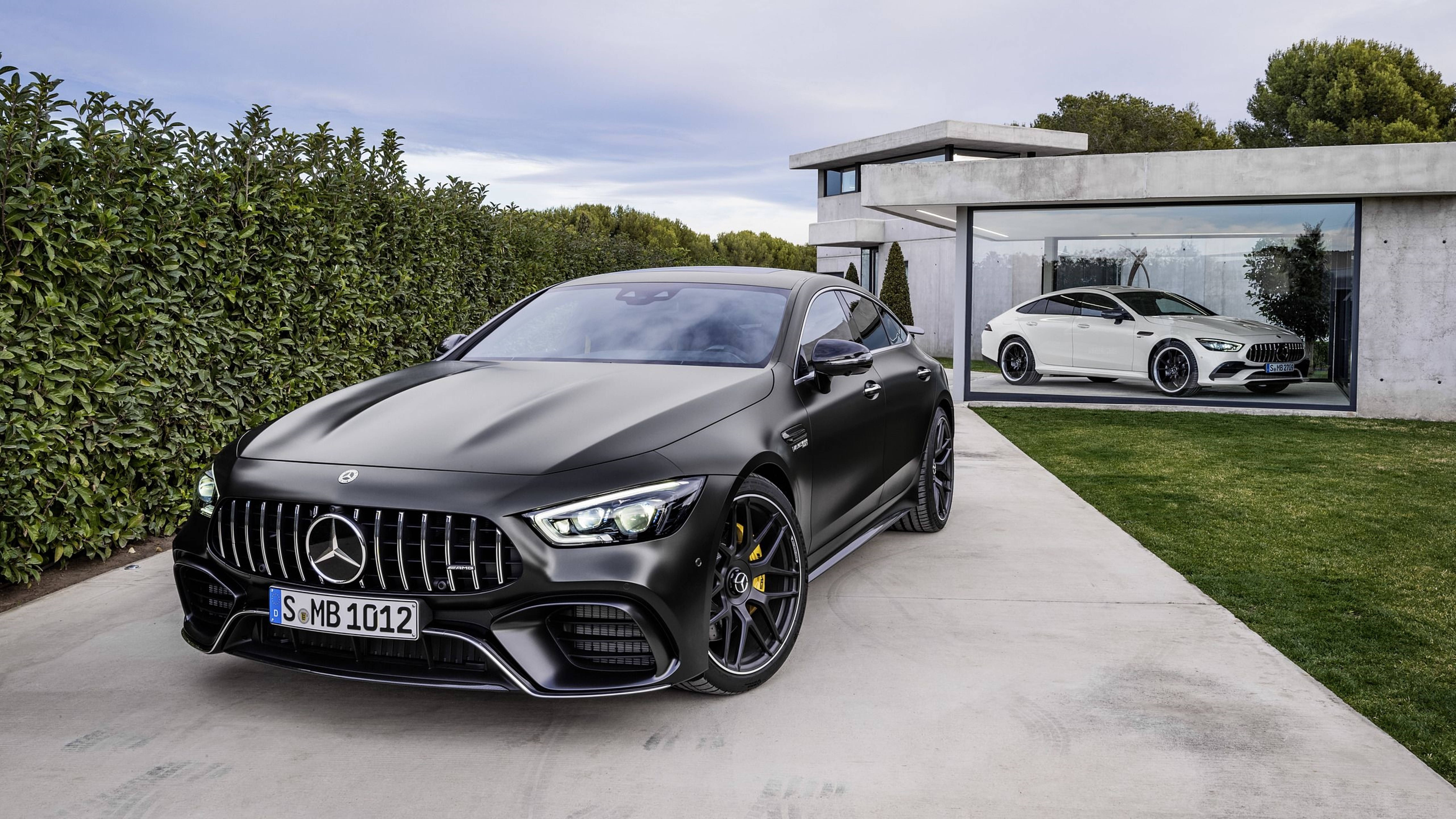 Mercedes 桌布 壁紙 — 一架時尚的啞光黑色 Mercedes-AMG GT 停泊在混凝土車道上，旁邊是現代玻璃車庫，露出白色 AMG GT。
