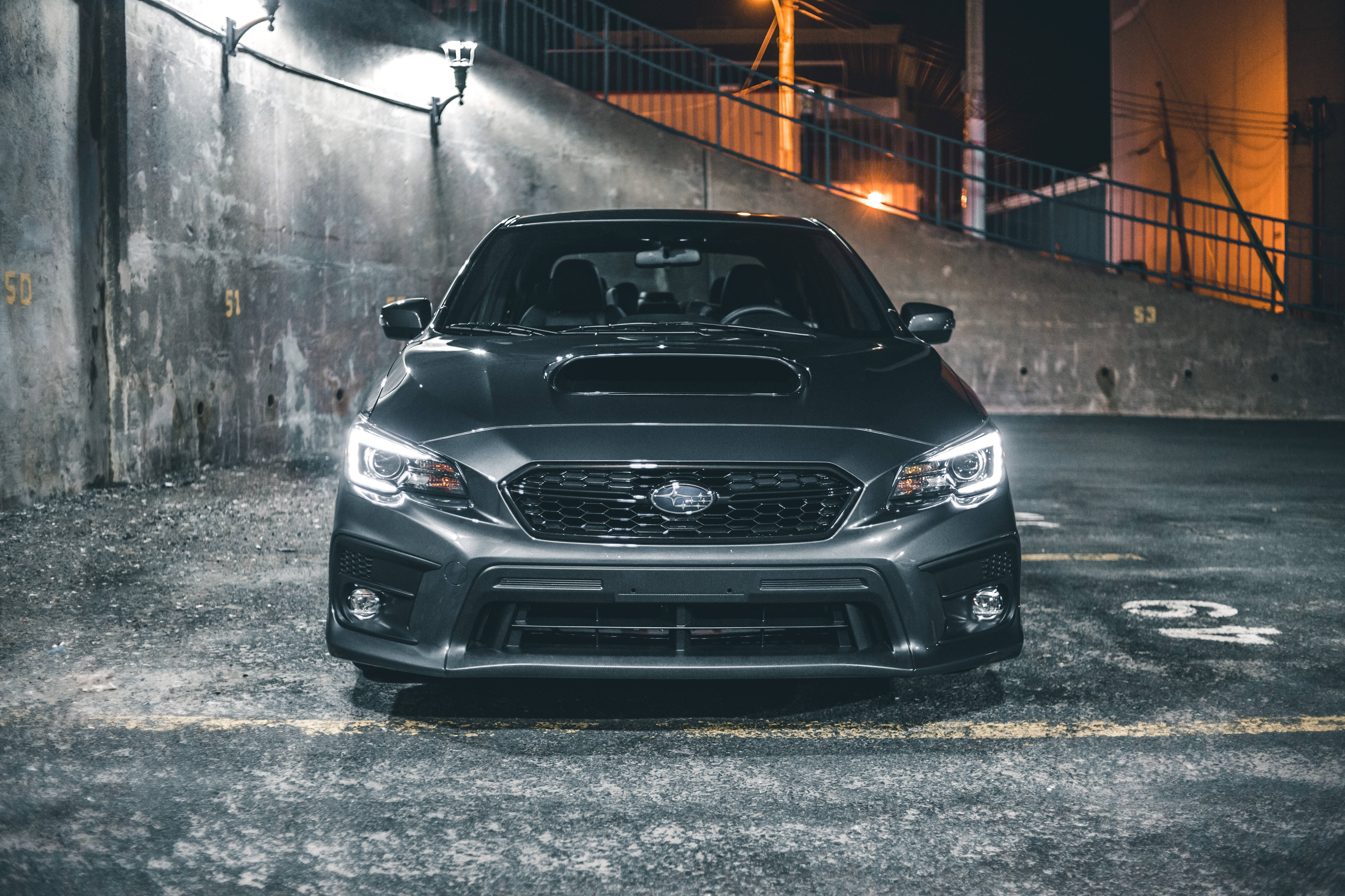 subaru 桌布 壁紙 — 一架時尚的啞光黑色Subaru WRX STI停泊在燈光昏暗的市區停車場，車頭燈閃爍發光。