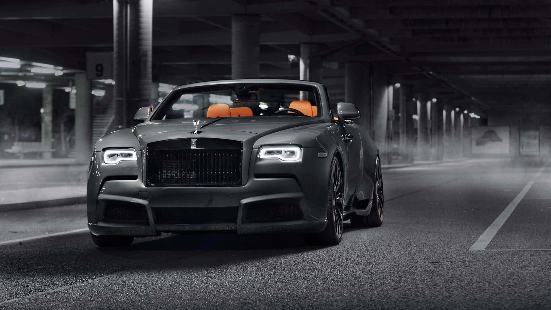 Rolls Royce 桌布 壁紙 — 一架時尚的啞光黑色勞斯萊斯敞篷車配橙色座椅，在霧氣瀰漫的地下停車場中滑行。