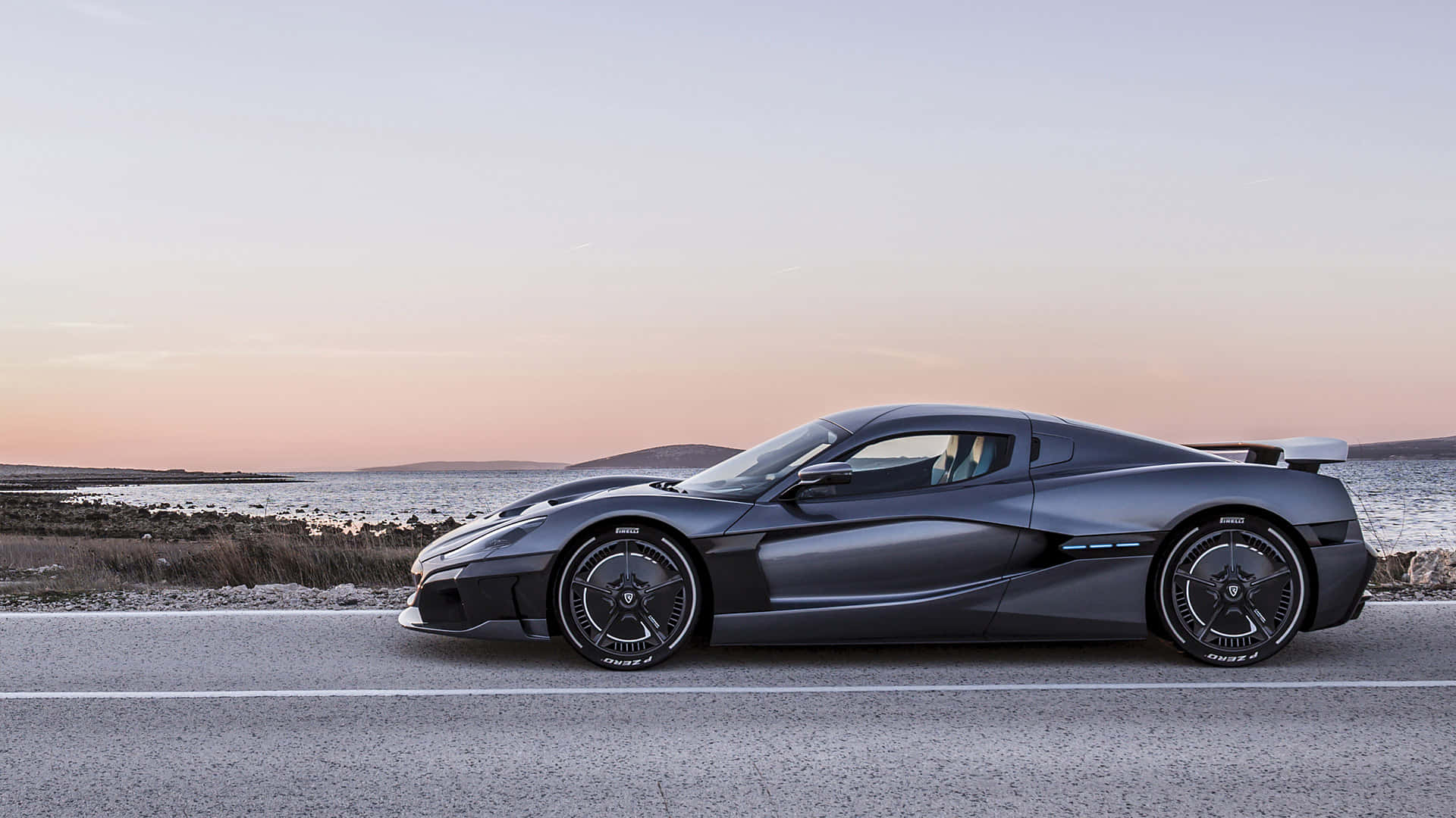 Rimac 桌布 壁紙 — 一架時尚的啞光黑色超跑停泊在日落時分的海岸公路上，天空呈現柔和的粉紅色和橙色。