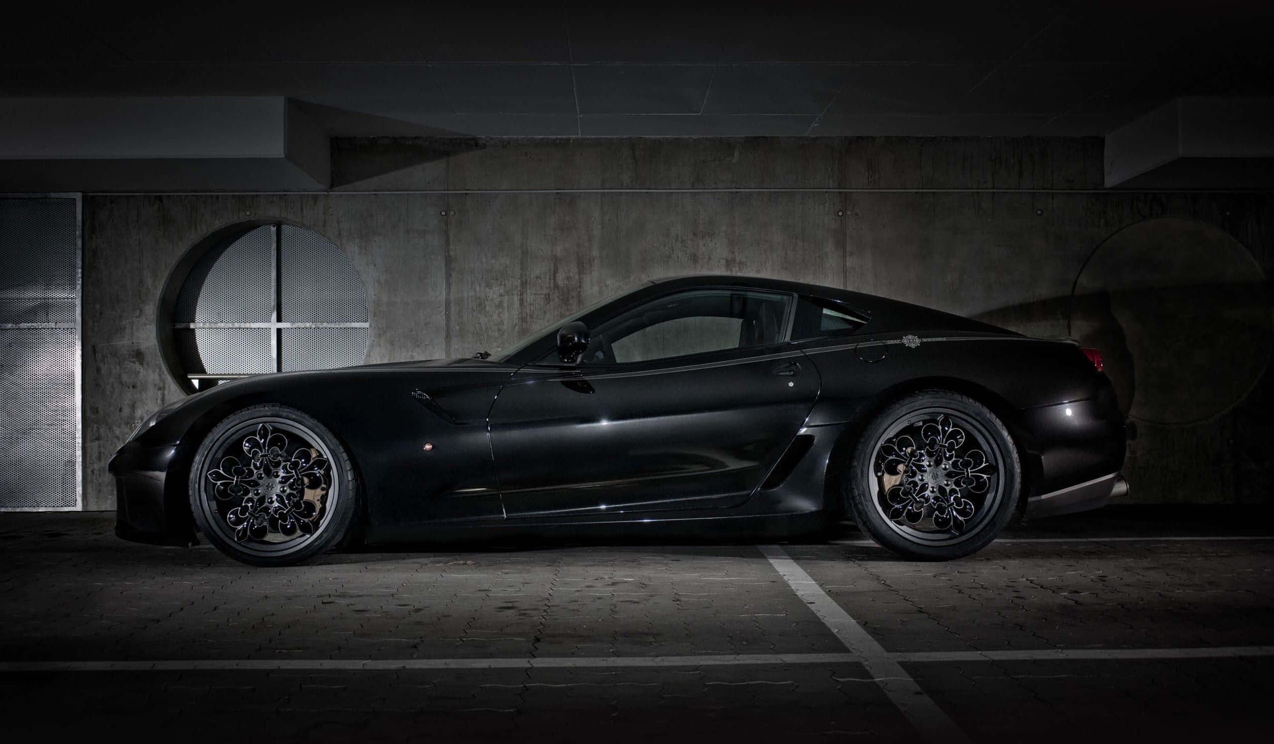 Ferrari 599 Gtb Fiorano 桌布 壁紙 — 一架時尚的啞光黑色跑車停放在光線昏暗的混凝土車庫中，帶有戲劇性的聚光燈照明。