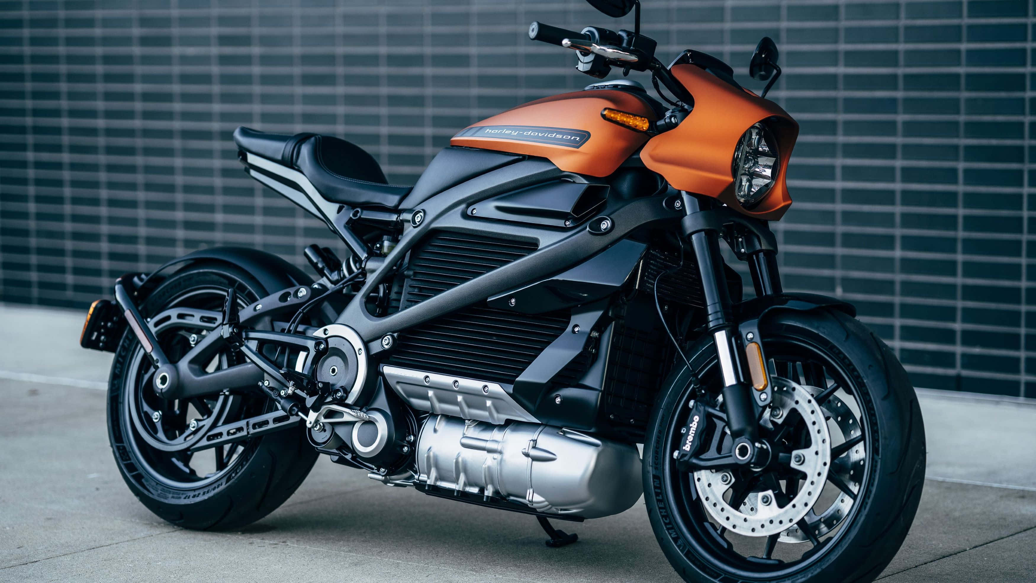 Electric Bike 桌布 壁紙 — 一架時尚的橙色和黑色Harley-Davidson電單車停泊在深灰色瓷磚牆前。
