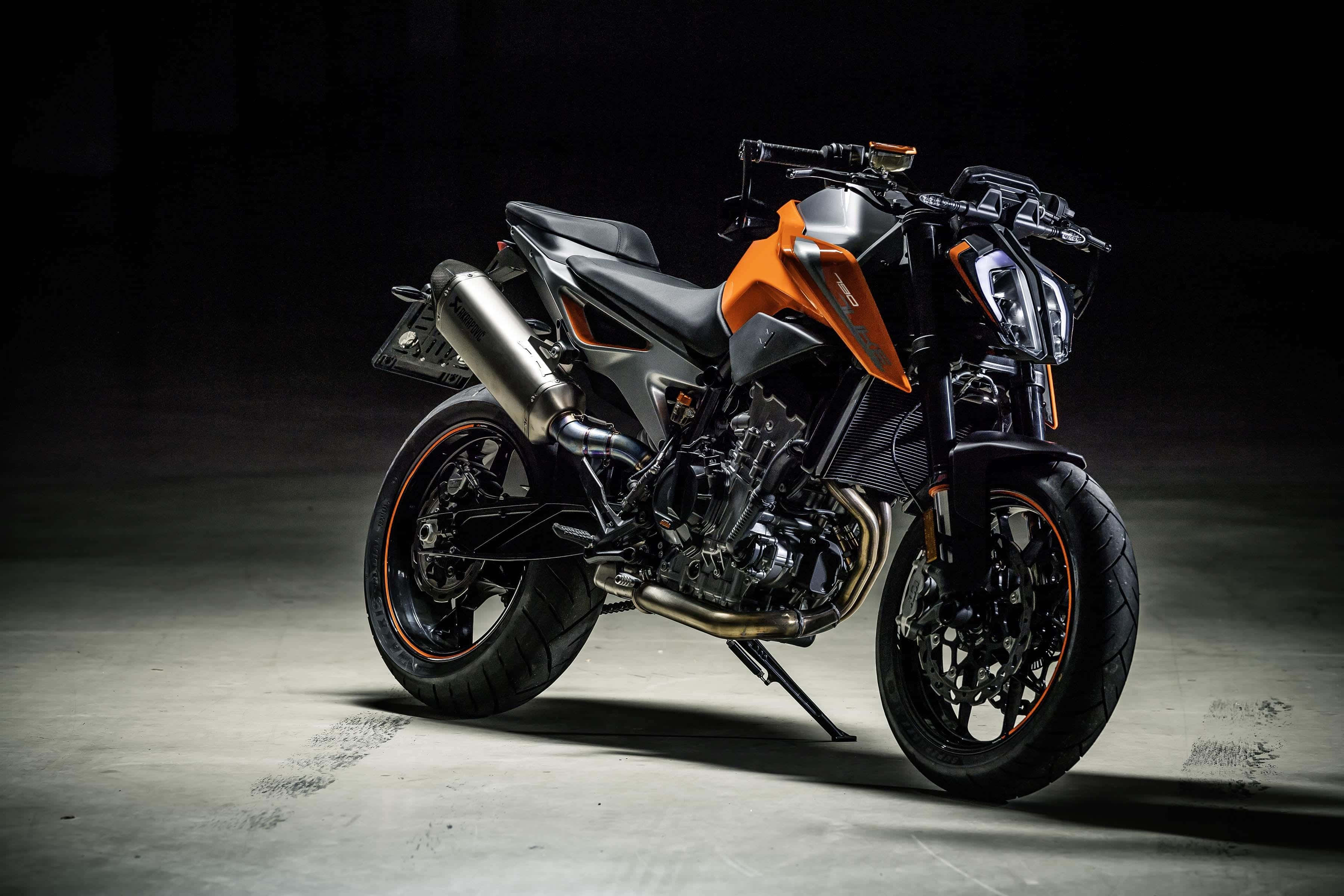 Ktm Bike 桌布 壁紙 — 一架時尚的橙色和黑色KTM電單車在黑暗的攝影棚地板上戲劇性地照亮，展示其侵略性設計和鍍鉻排氣管。