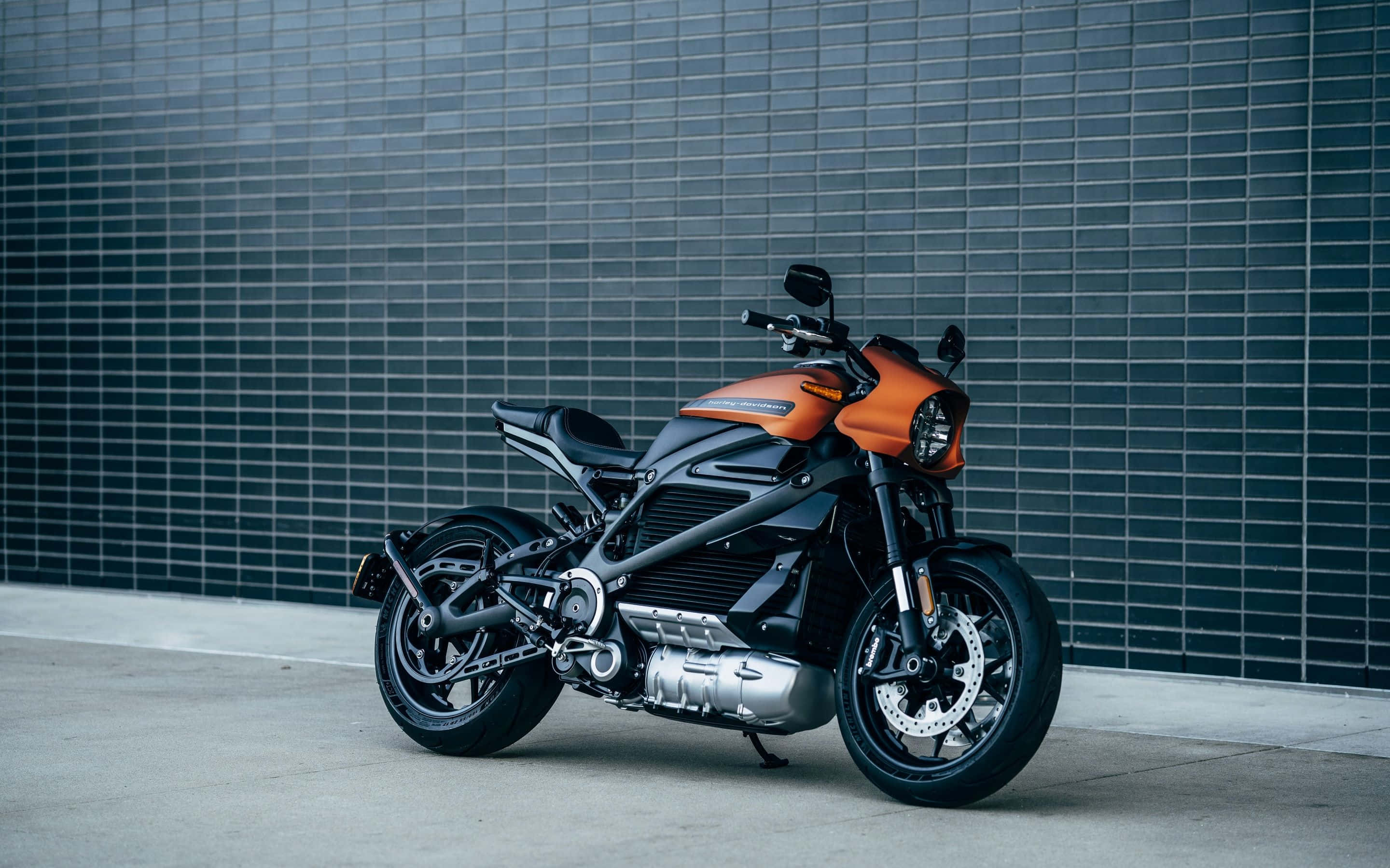 Electric Bike 桌布 壁紙 — 一架時尚的橙色和黑色電動電單車，在混凝土表面上靠著深色瓷磚牆擺好姿勢。