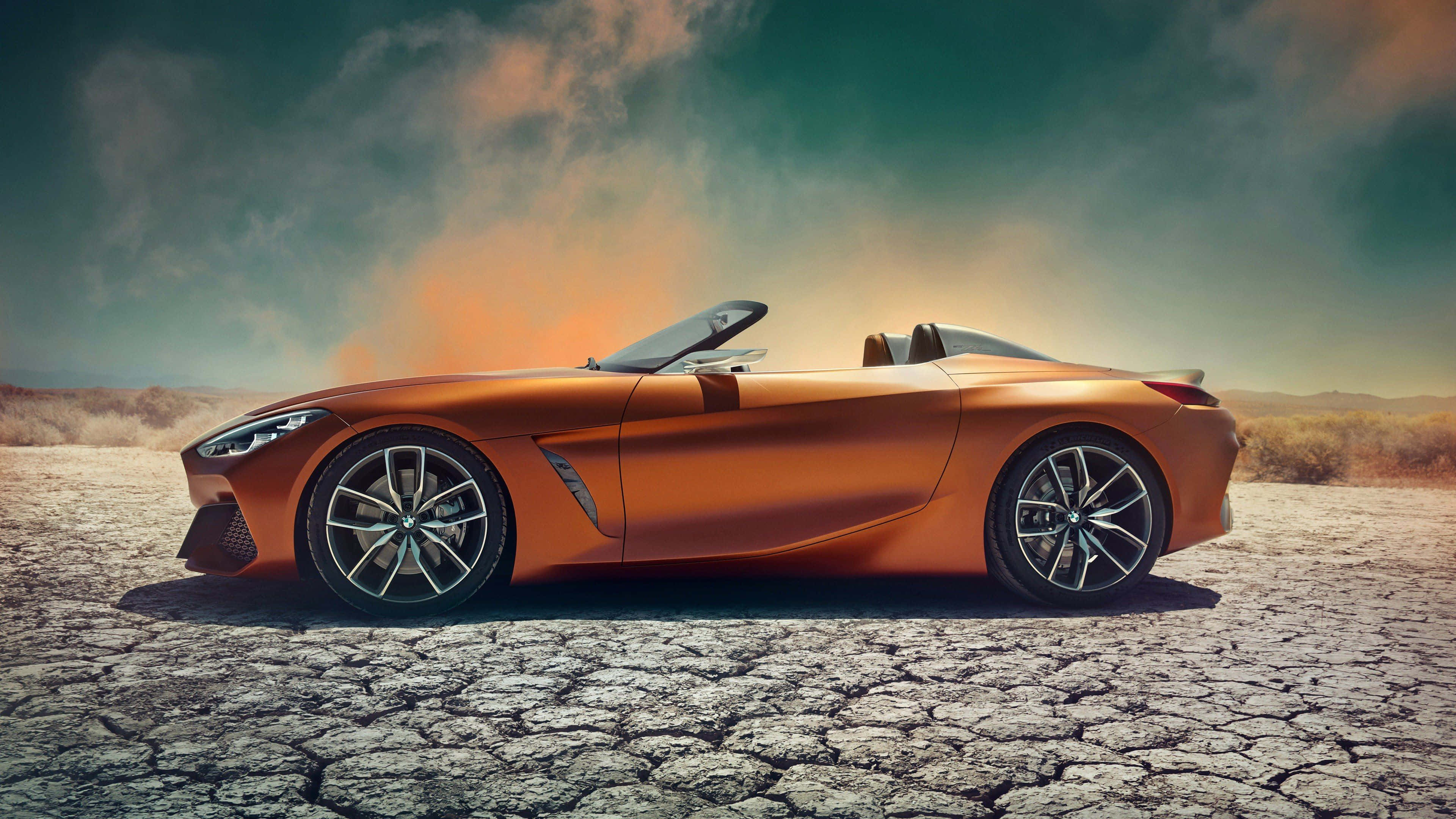 Bmw Z4 桌布 壁紙 — 一架時尚的橙色開篷跑車停泊在龜裂的沙漠土地上，背景是戲劇性的暮色天空。