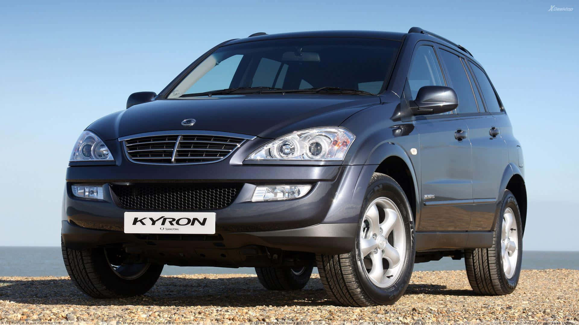 Ssangyong 桌布 壁紙 — 一架時尚的深灰色Kyron SUV停泊在卵石海灘上，背景是海洋和清澈的藍天。