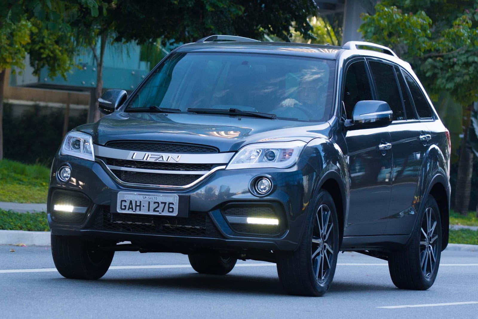 Lifan 桌布 壁紙 — 一架時尚的深灰色力帆SUV停泊在林蔭大道上，陽光在其拋光表面上閃爍。